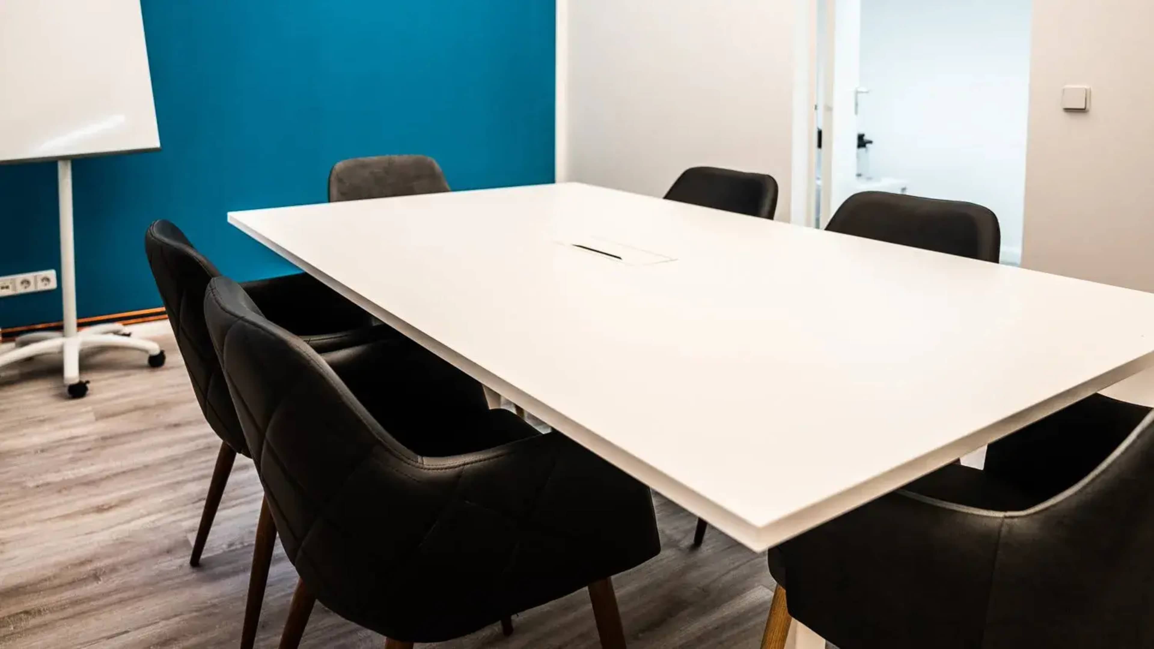 The image shows a modern conference room with a large white table surrounded by black chairs and a blue accent wall.