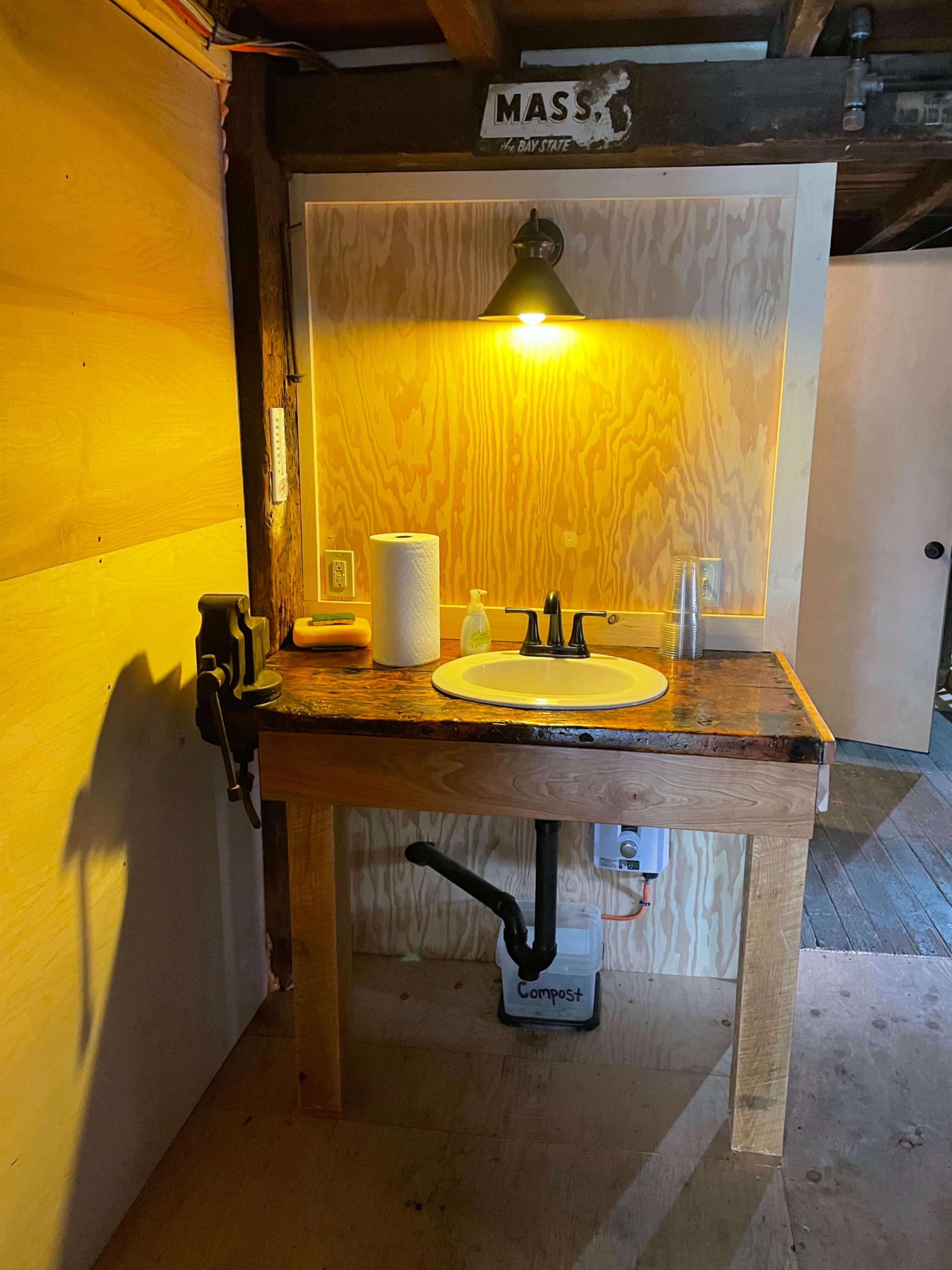 A wooden countertop with a sink, faucet, and various cleaning supplies under a warm light in a rustic bathroom setting.