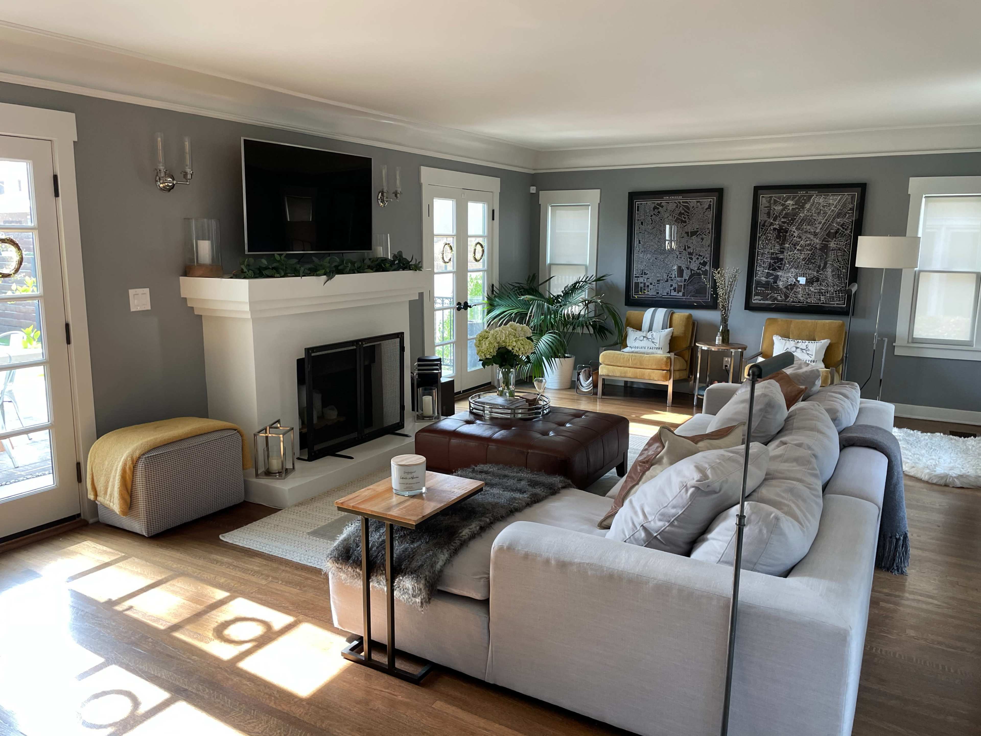 The living room features a neutral color palette with a large sectional sofa, a coffee table, a fireplace, and two armchairs, all arranged around a central area with natural light coming in through the windows.