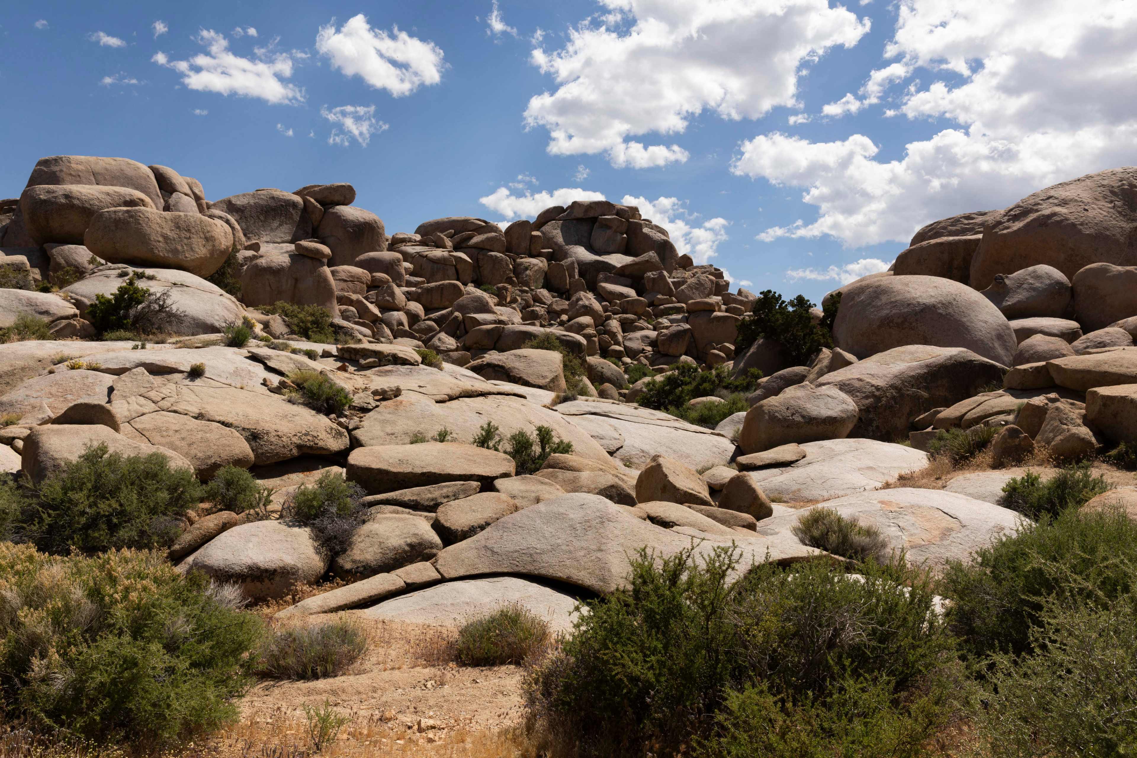 A rocky landscape features large boulders and sparse vegetation under a partly cloudy sky.