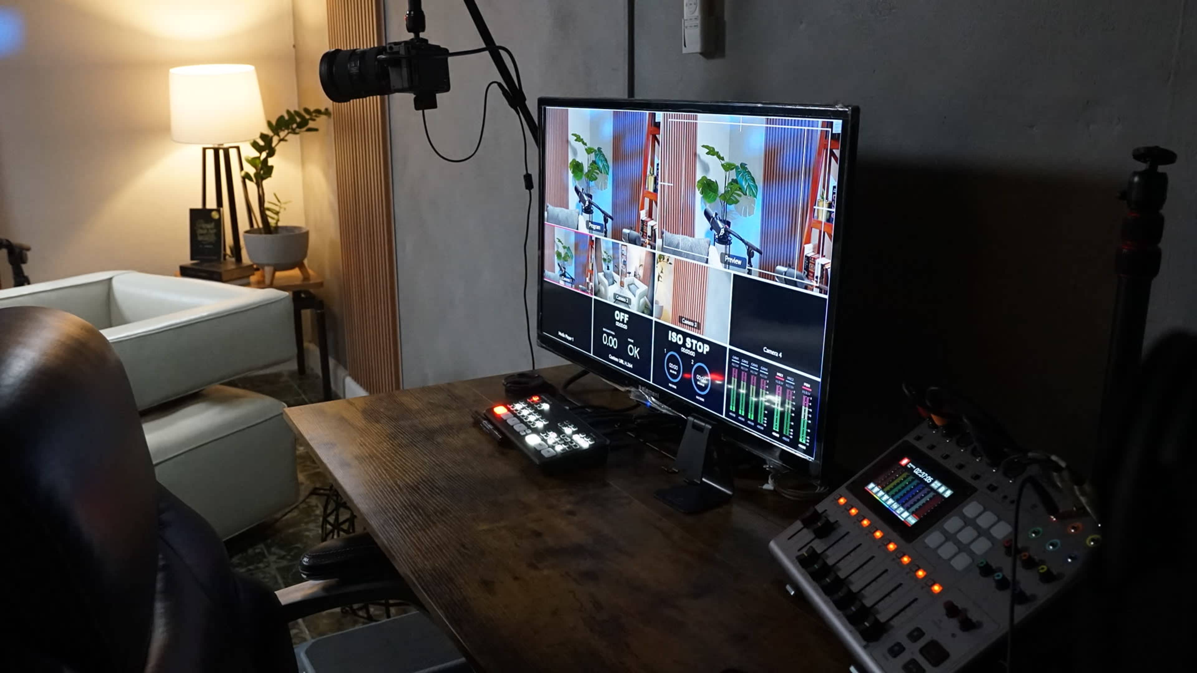 A television monitor displays multiple camera feeds in a recording studio, complemented by a microphone and sound control equipment on a wooden desk.