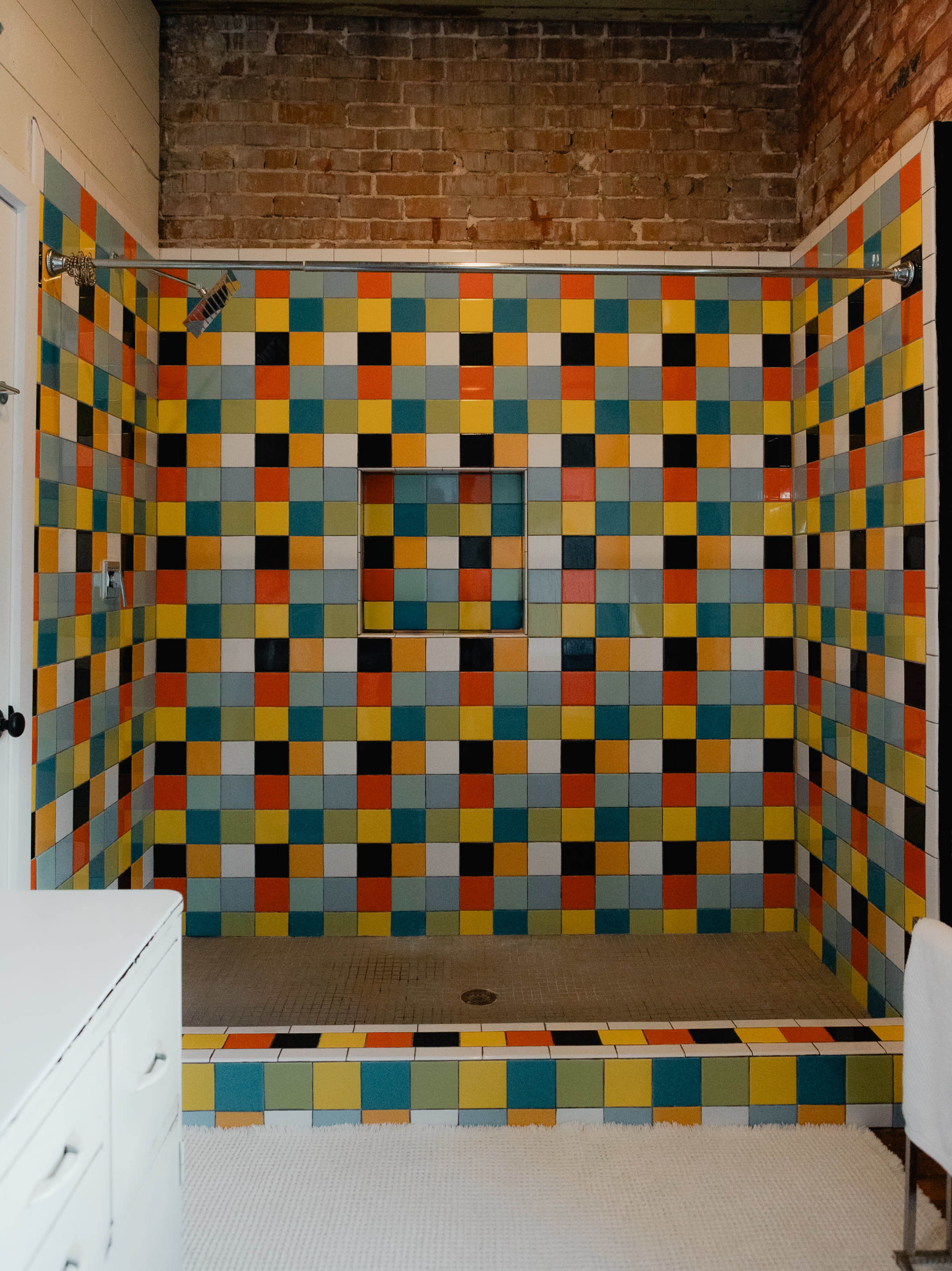 The image features a colorful tiled shower with a geometric pattern of squares on the walls, illuminated by natural light.