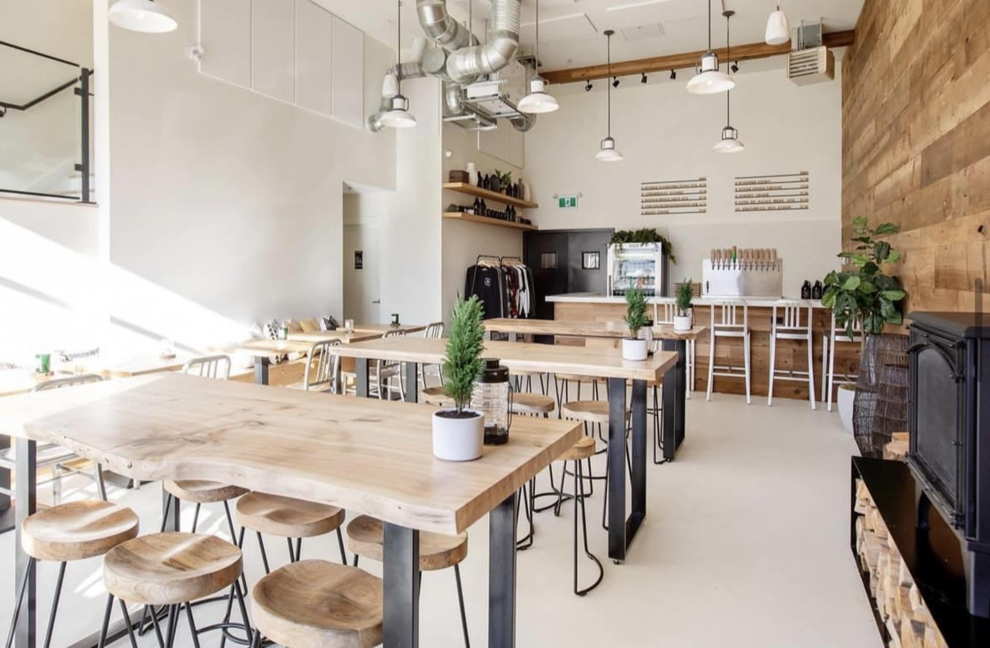 A modern, minimalist café with wooden tables, metal chairs, and a prominent wooden wall, illuminated by overhead lights.