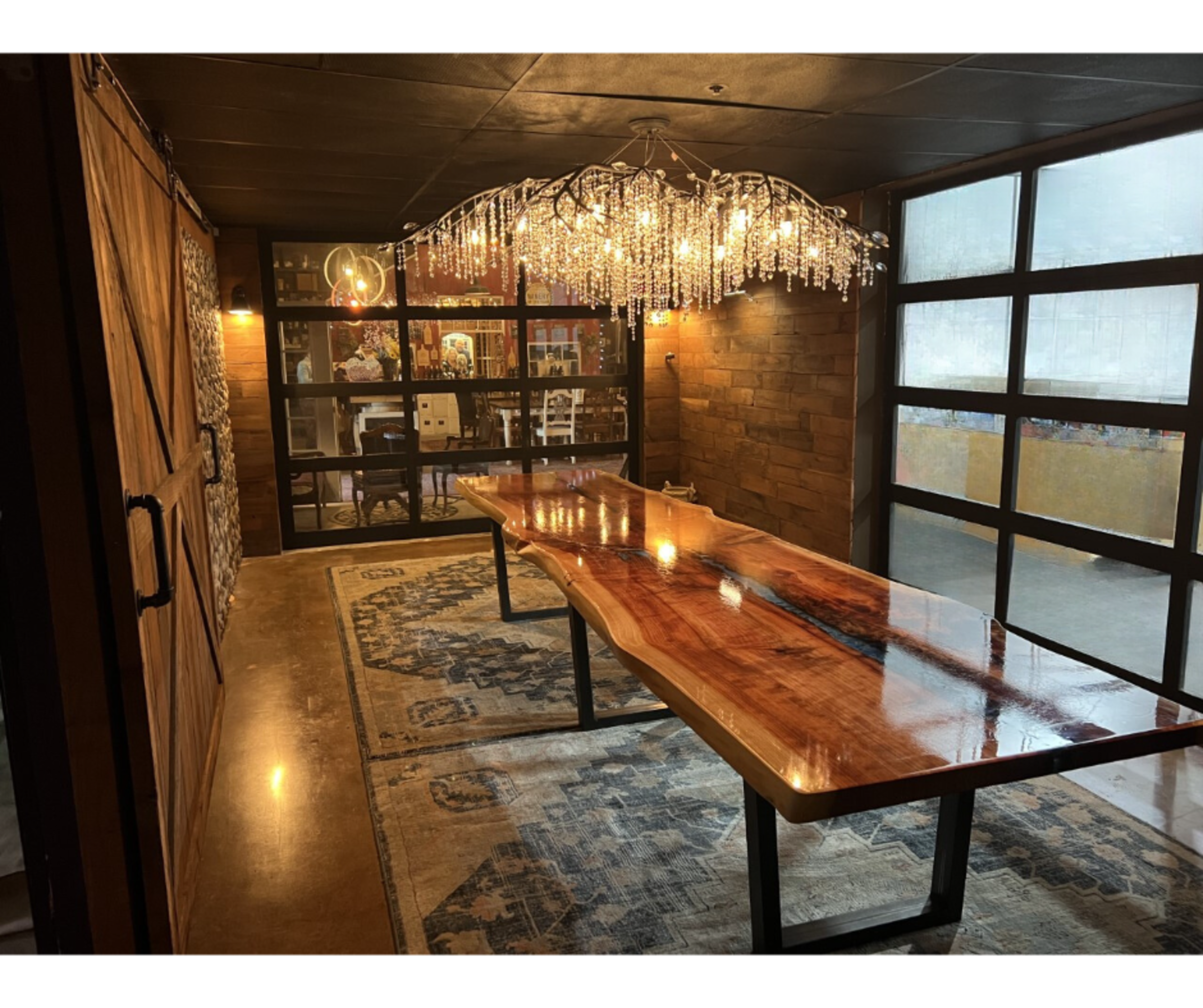 A spacious dining area featuring a large wooden table with a glossy surface, complemented by a crystal chandelier and large windows.
