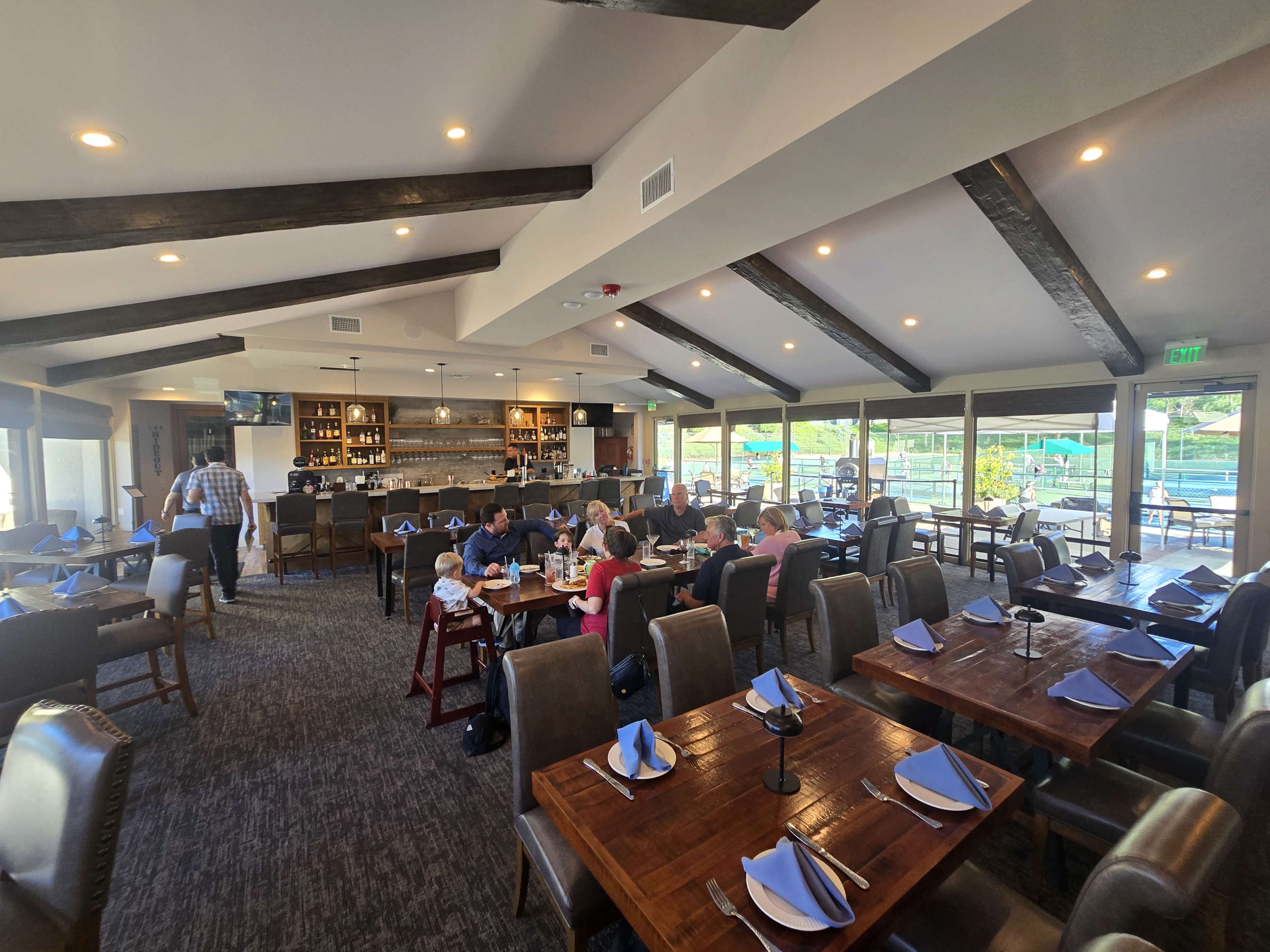 The image shows a spacious restaurant interior with wooden beams and tables arranged for dining, occupied by families and patrons.