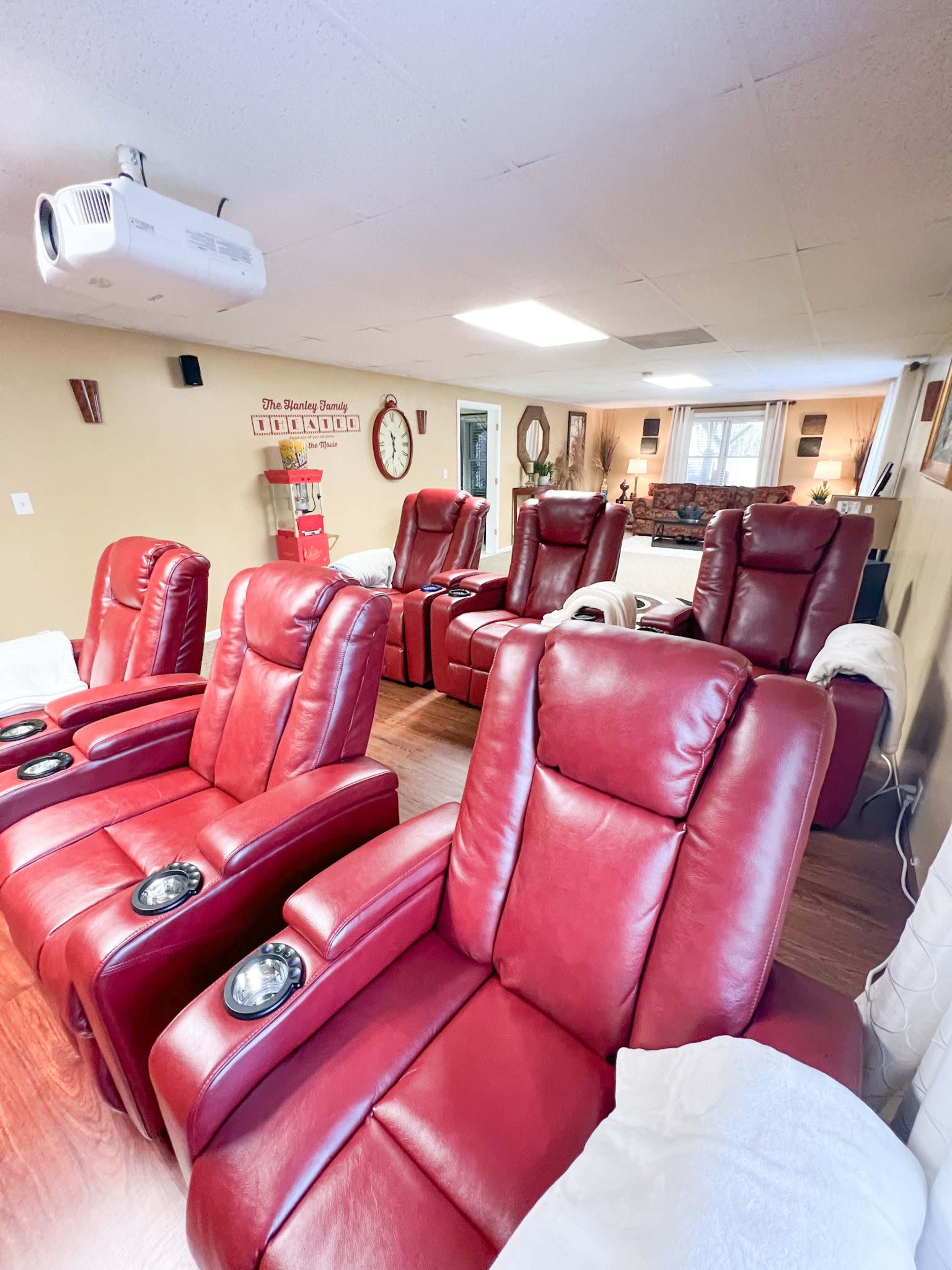 A room with several red reclining chairs arranged in rows, equipped with cup holders and a projection screen on the ceiling.