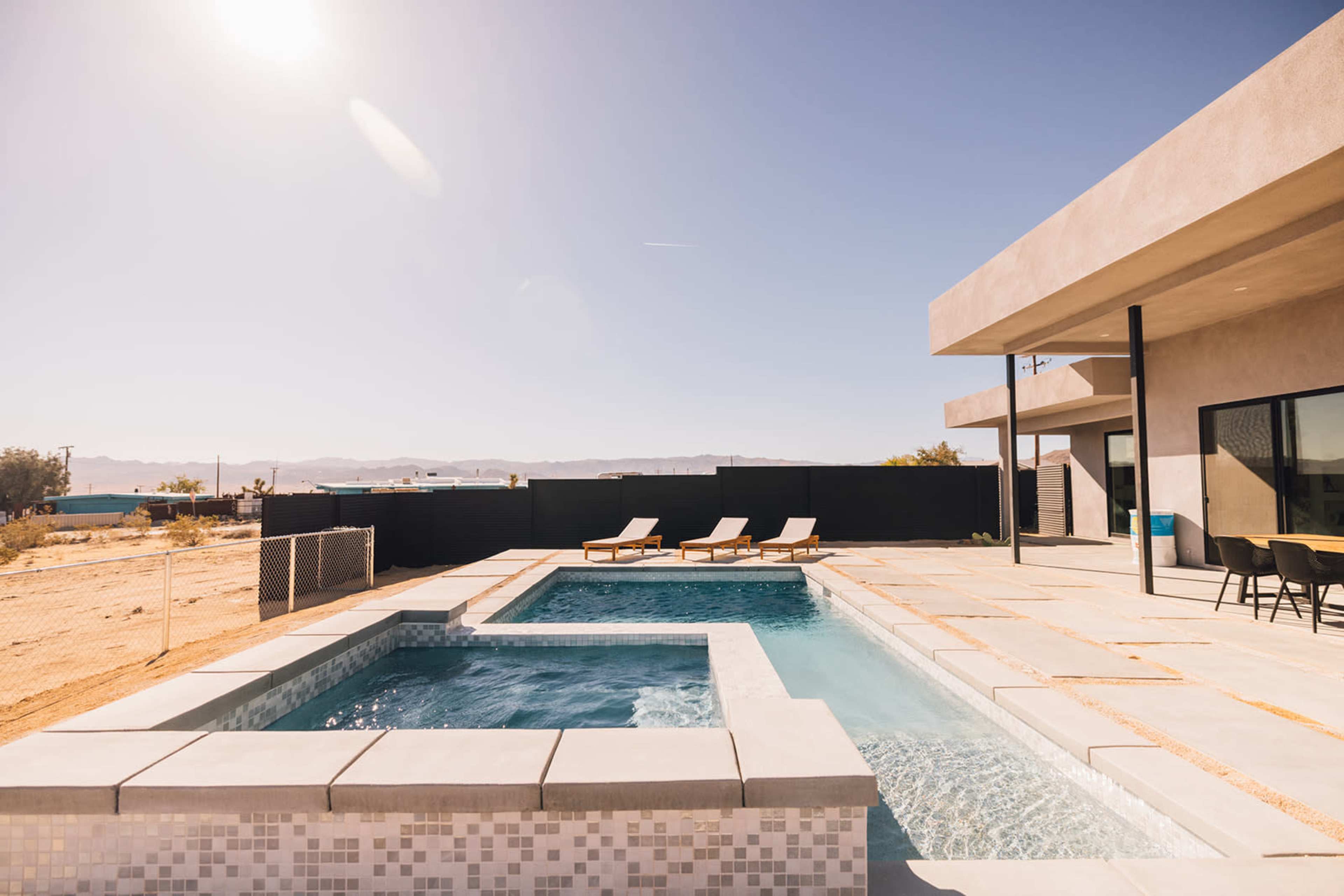 A modern outdoor space featuring a swimming pool and a hot tub, with lounge chairs positioned nearby against a desert backdrop.