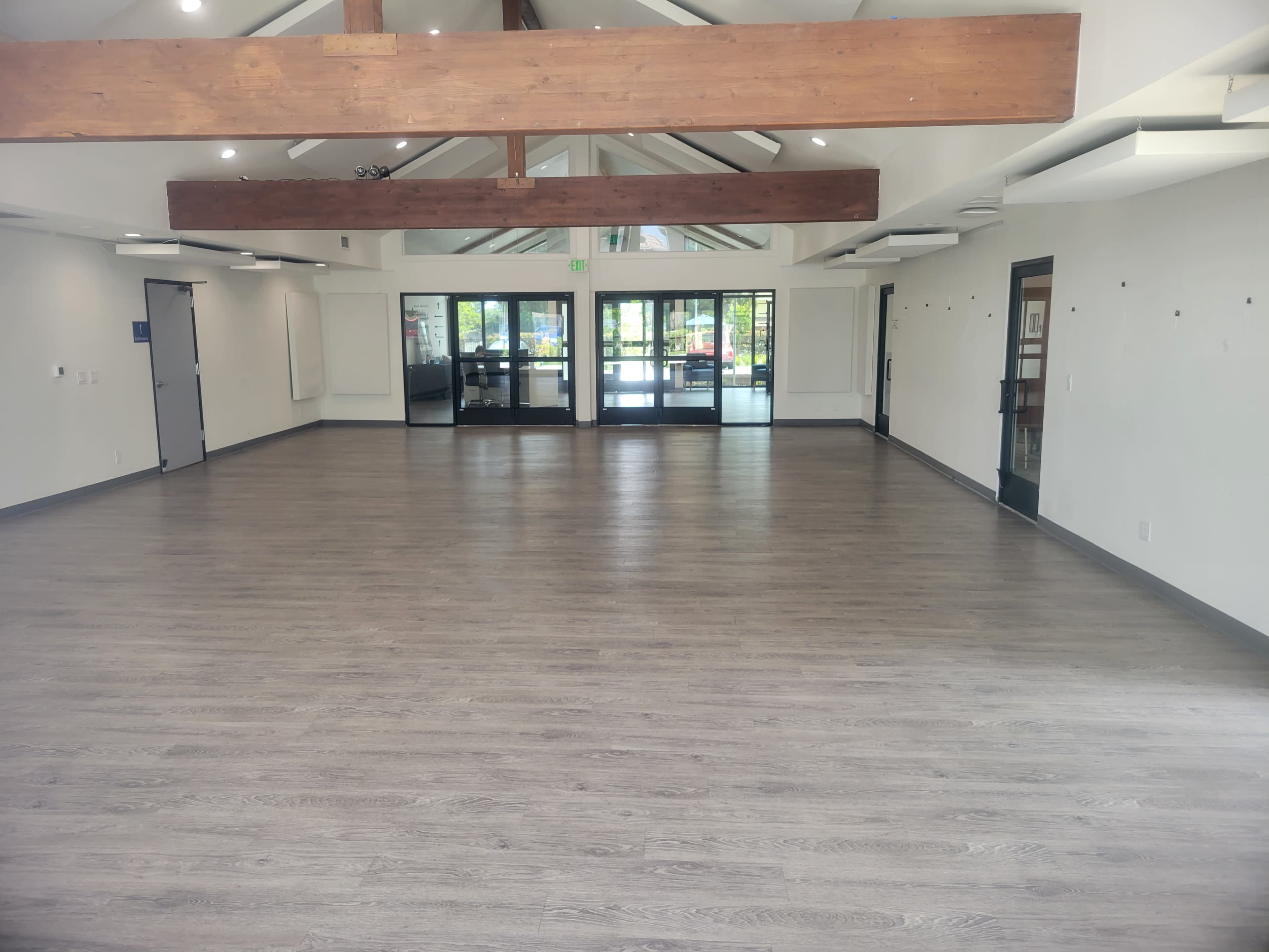 A spacious room with wooden beams, light-colored flooring, and large glass doors leading to an outdoor area.