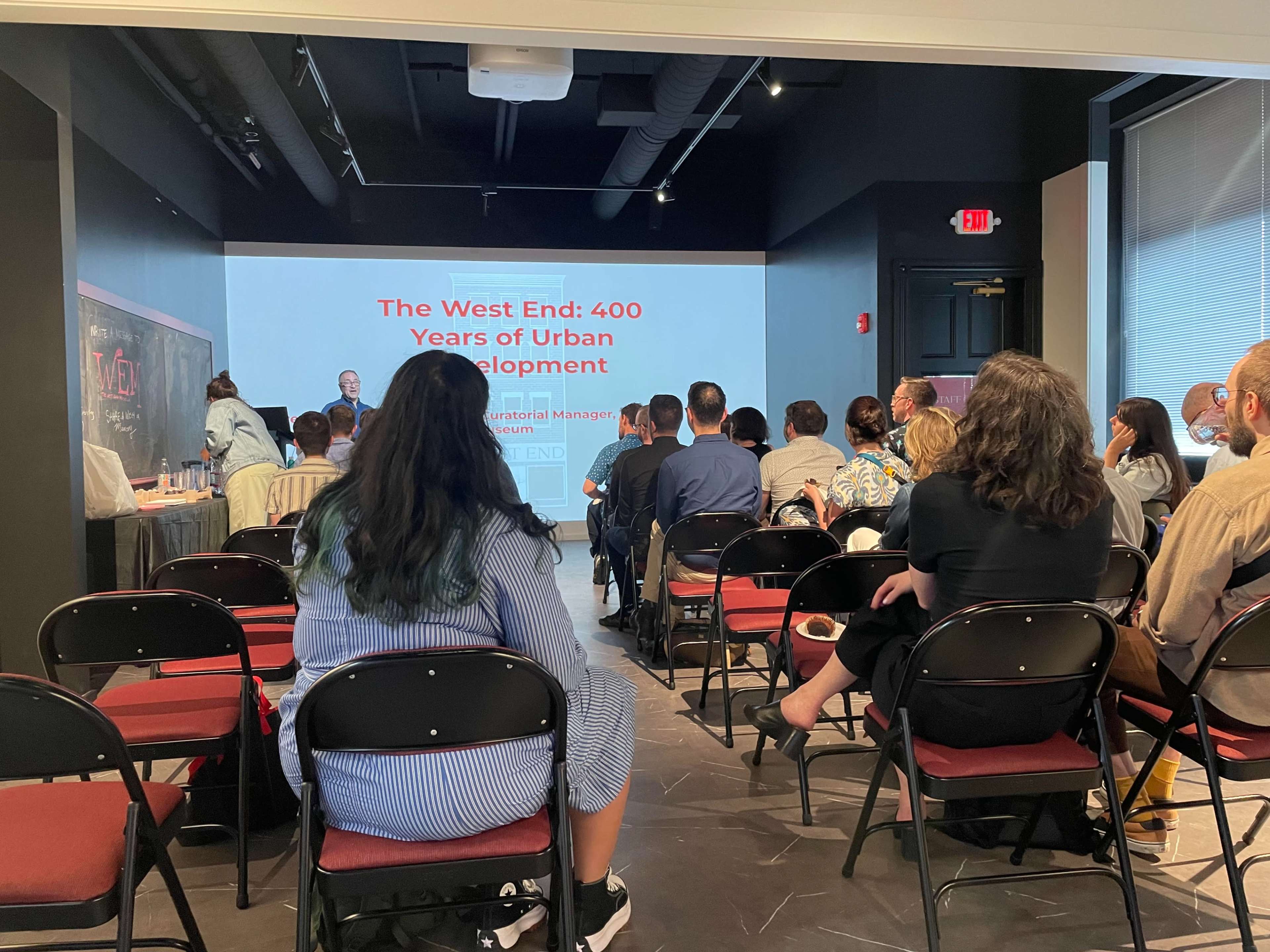 A group of attendees is sitting in a meeting room while listening to a presentation titled "The West End: 400 Years of Urban Development."