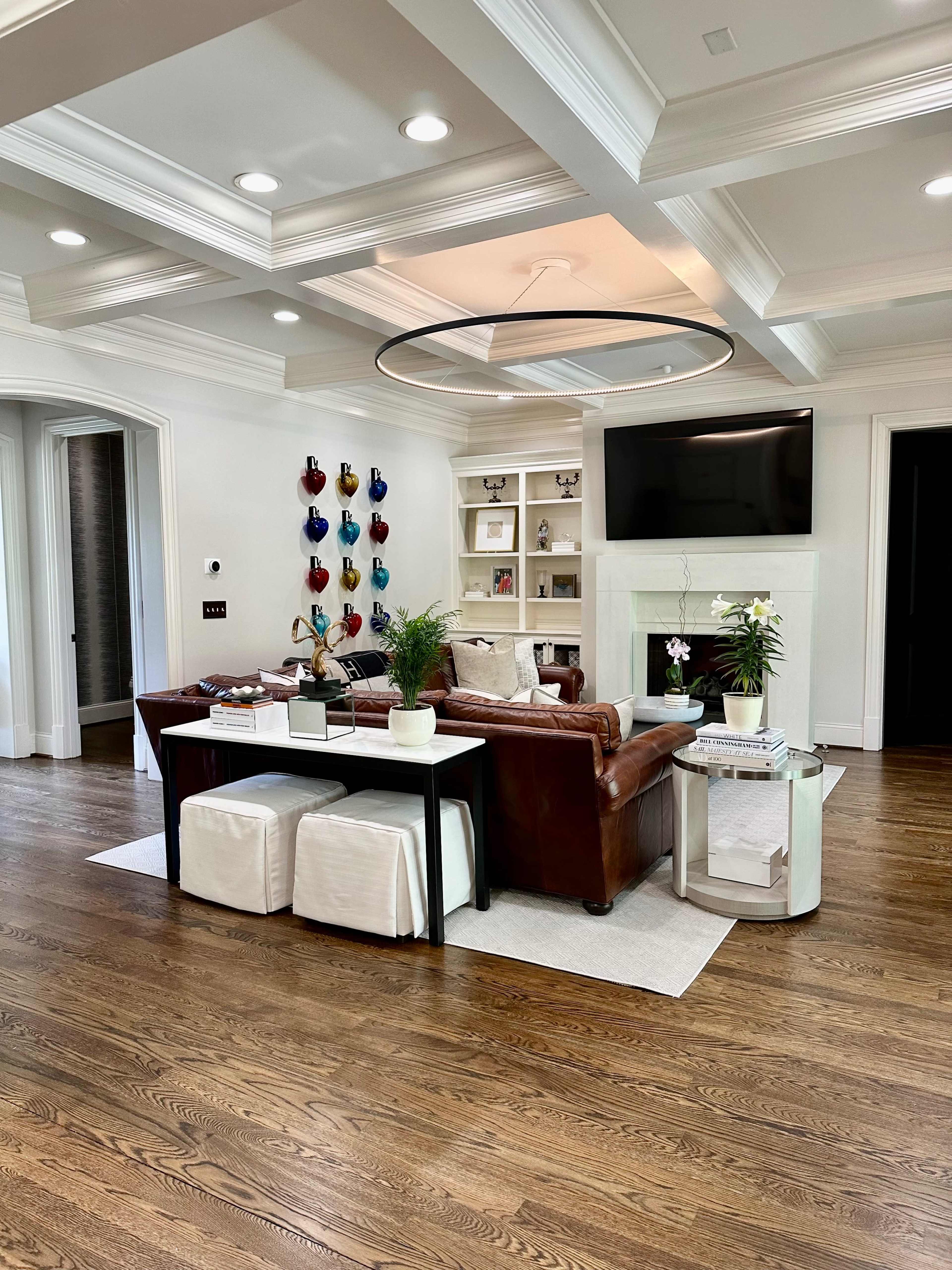 The image shows a modern living room featuring a leather sofa, a coffee table with decorative items, and a large flat-screen TV mounted above a white fireplace, all illuminated by recessed lighting.