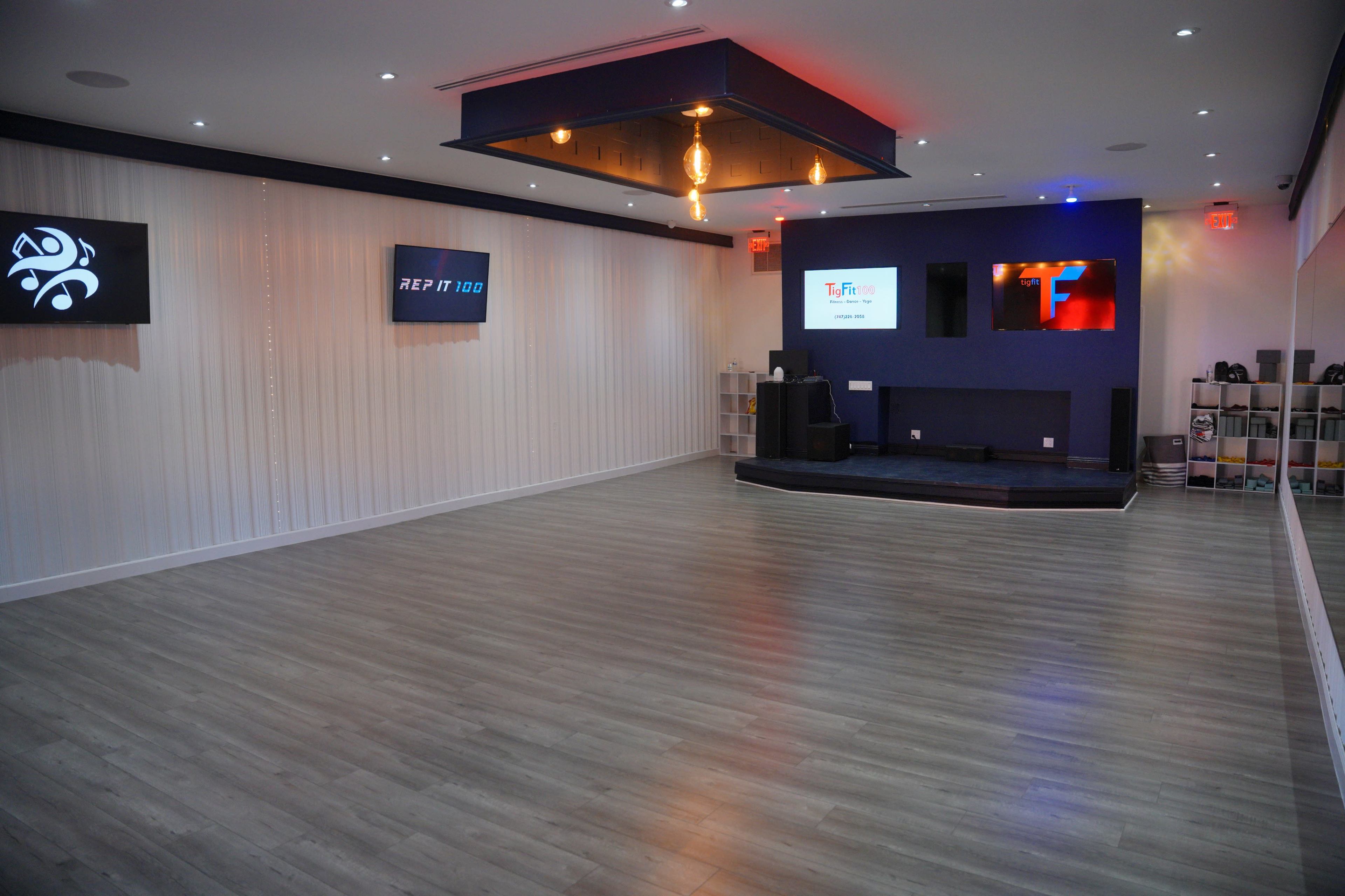 The image shows a spacious, modern studio interior with light wooden flooring, illuminated by ambient lighting and featuring screens mounted on the walls.