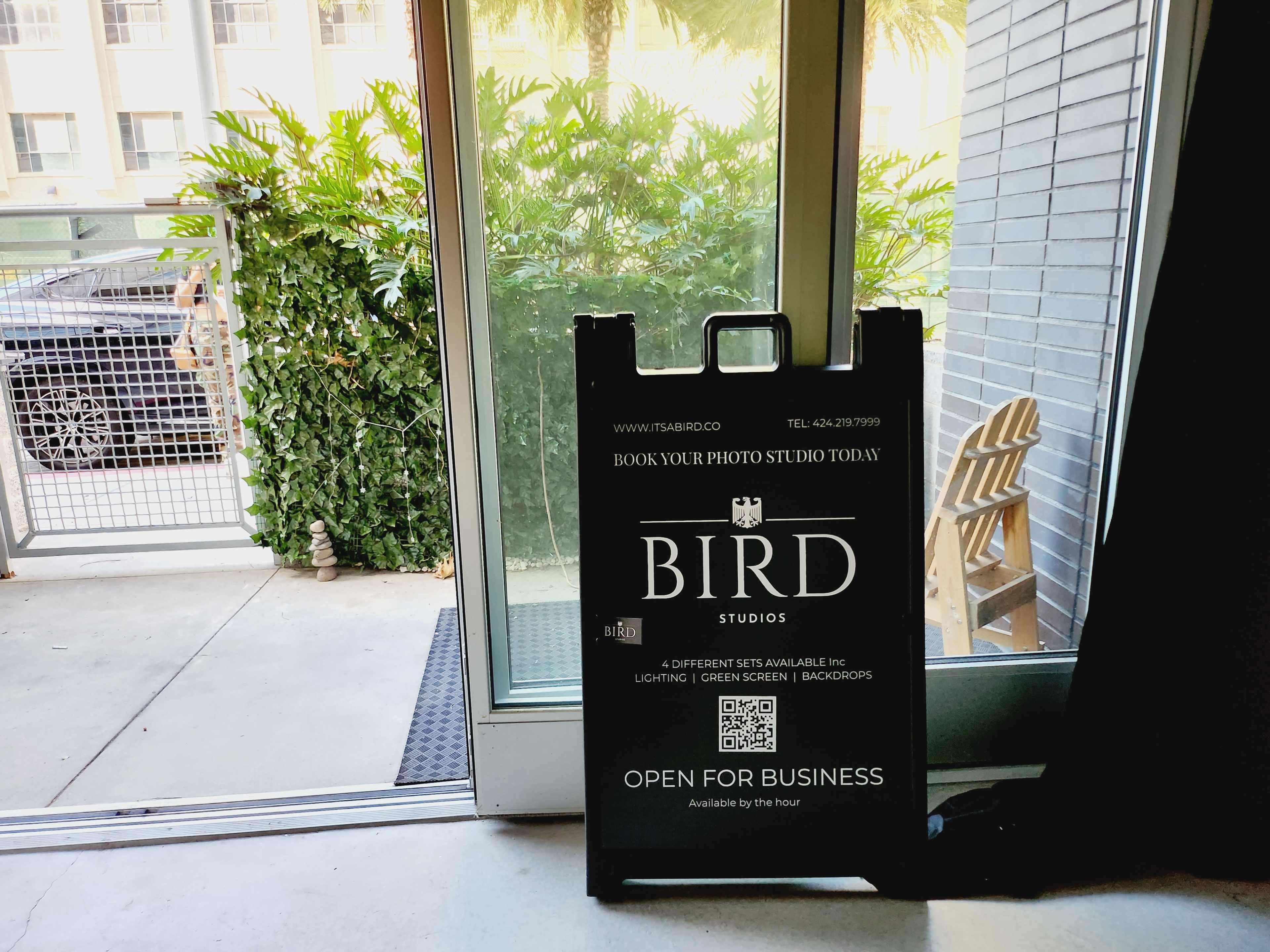 A sidewalk sign for Bird Studios is placed near a doorway, promoting photo studio bookings and displaying a QR code.