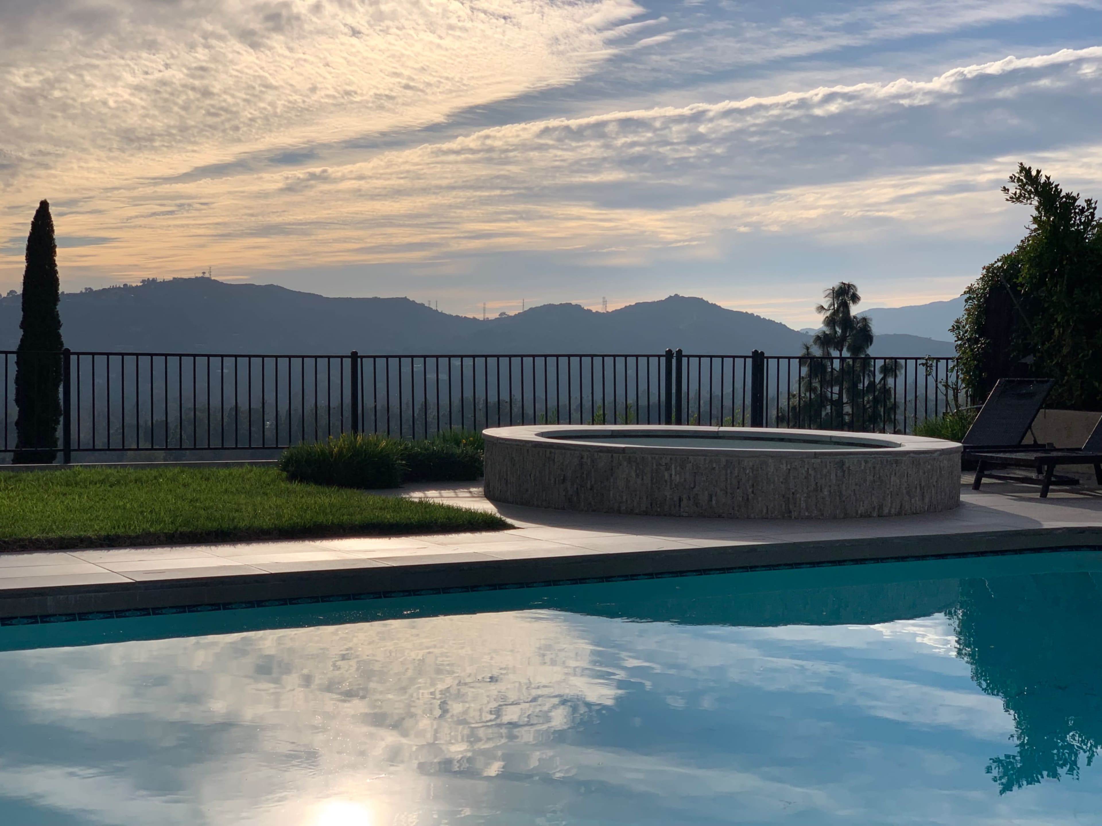 A tranquil pool area with a round spa, overlooking mountains and a cloudy sky.
