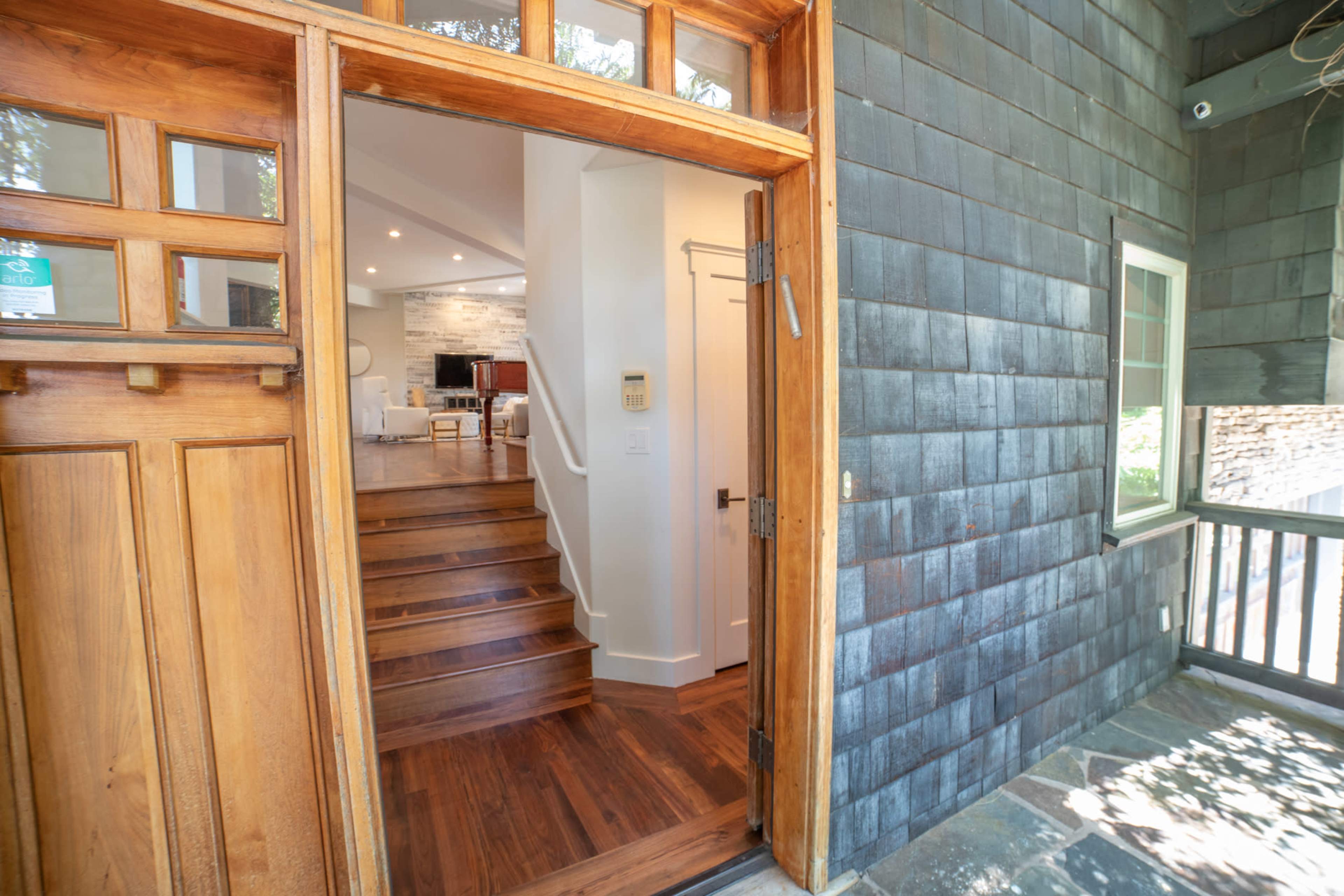 The image shows an entryway with a wooden door leading into a home with visible stairs ascending to an interior space.