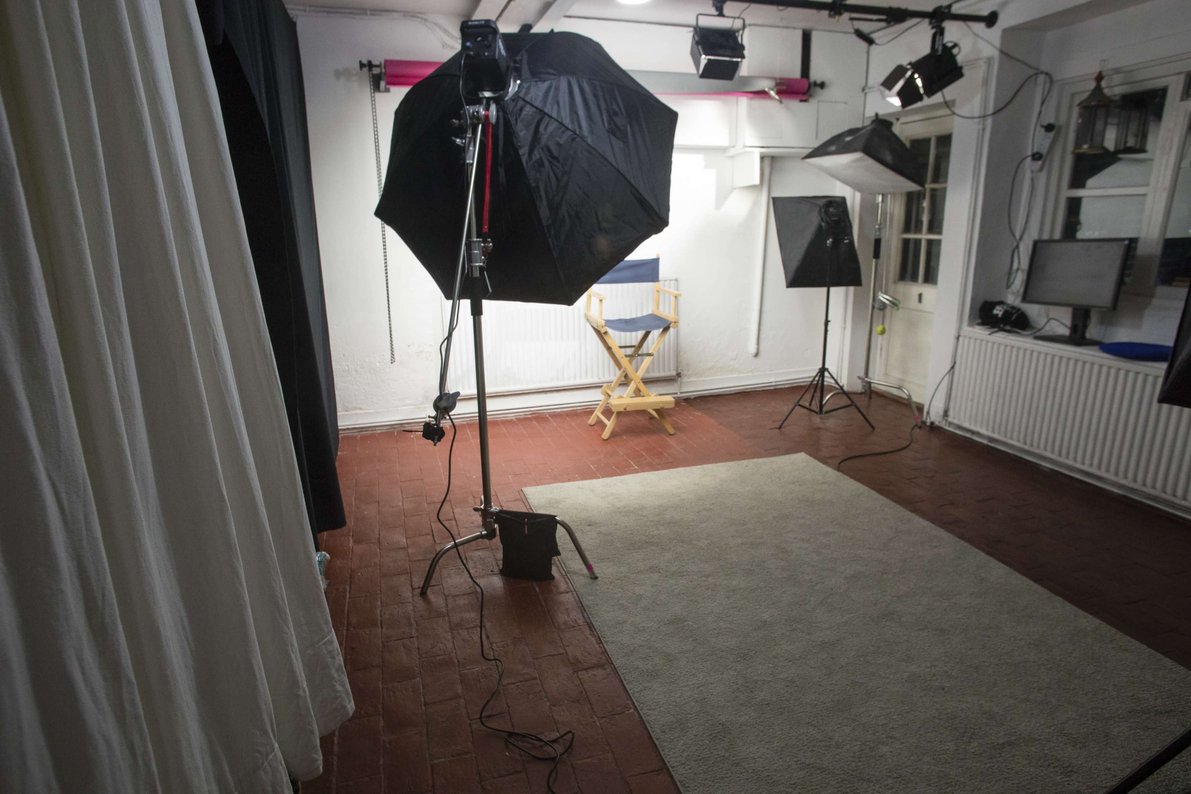 A photography studio setup with various lighting equipment, a director's chair, and a rug on the floor.