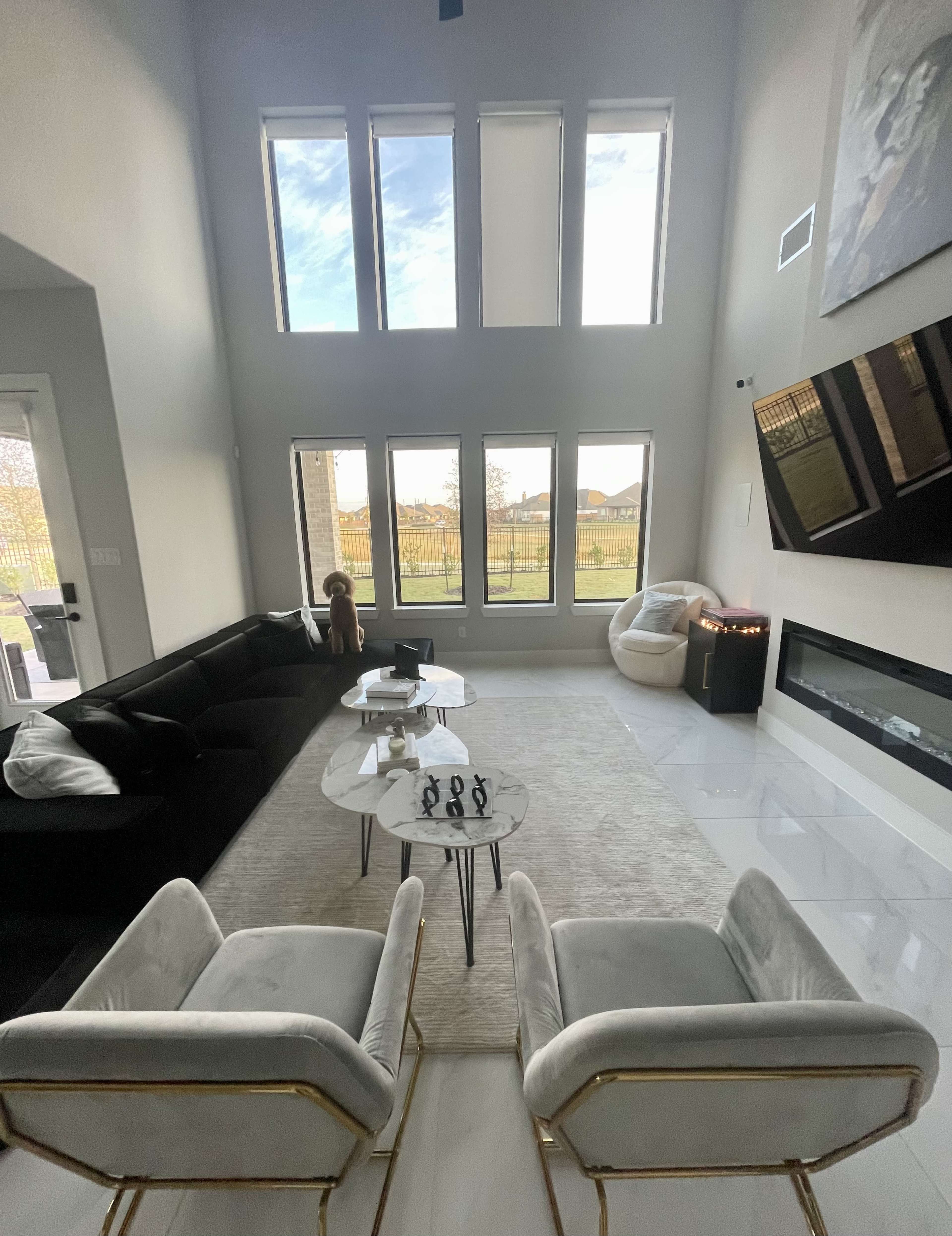 The interior of a spacious living room features modern furniture, large windows providing natural light, and a fireplace along one wall.