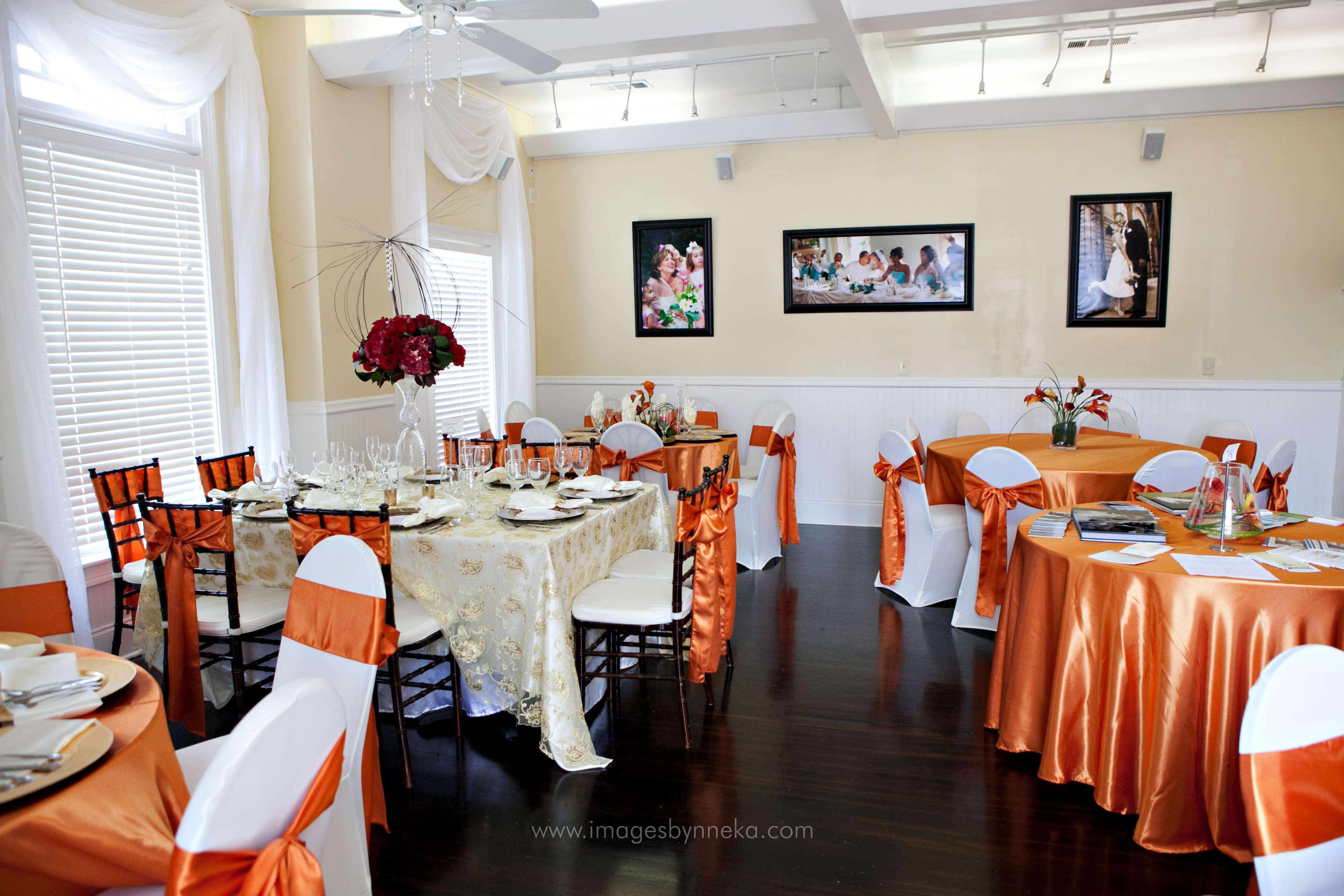 A banquet room set with tables dressed in orange and cream linens, decorated with floral centerpieces and dining ware.