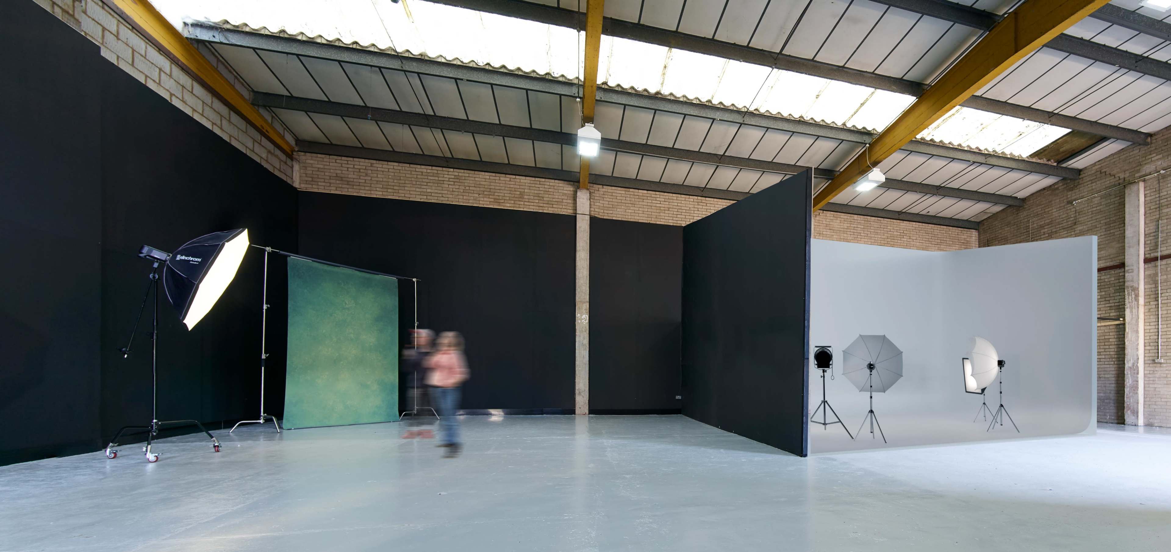 A spacious photography studio featuring a green backdrop and a white backdrop, with lighting equipment set up on the sides.