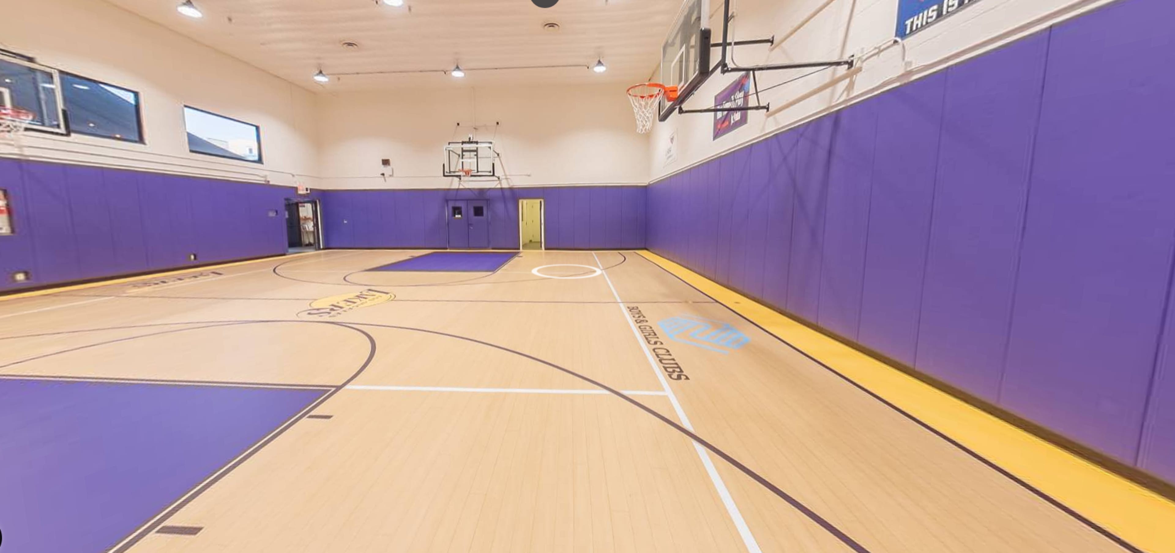 A basketball court with purple walls, two basketball hoops, and a smooth wooden floor marked with court lines.