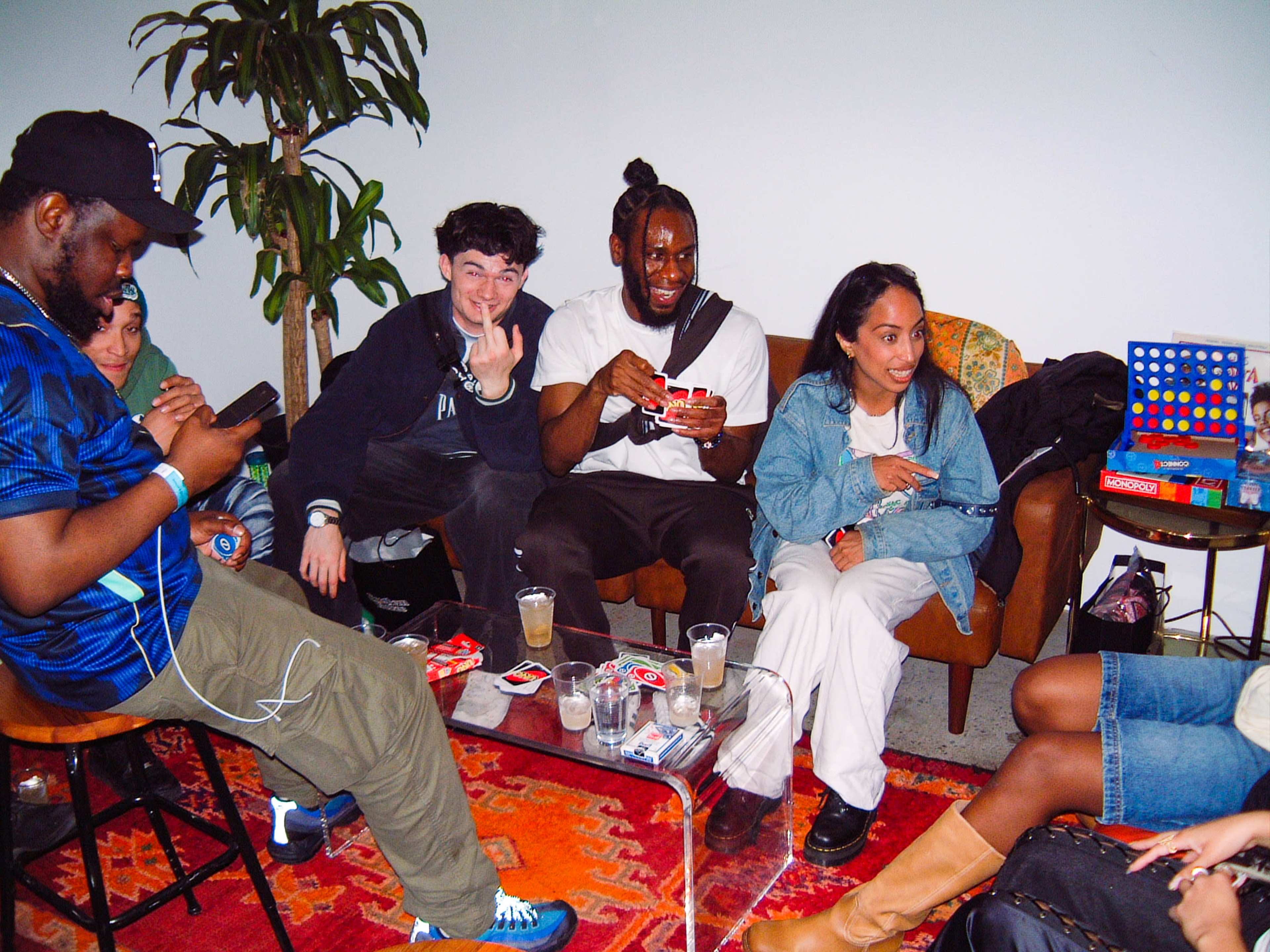 A group of five people are seated in a relaxed setting, engaging in conversation and playing games on a colorful rug.