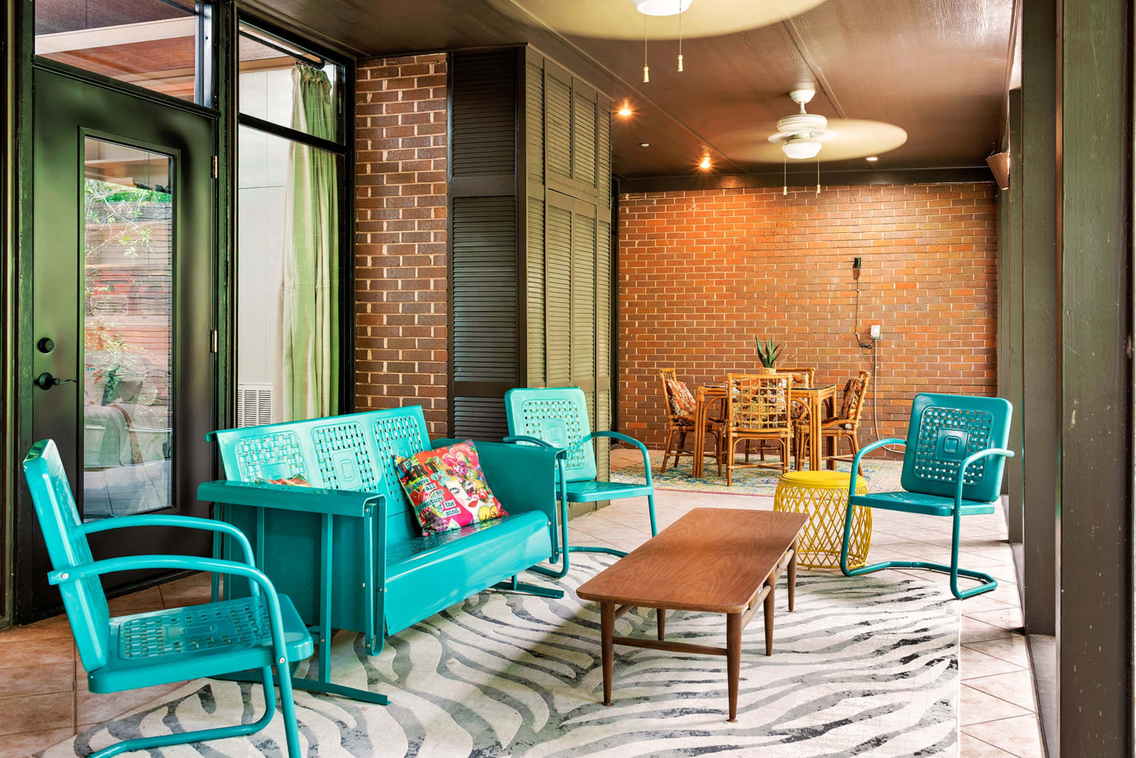 The image shows a screened-in porch with turquoise metal furniture, a wooden coffee table, and a dining area illuminated by warm lighting.