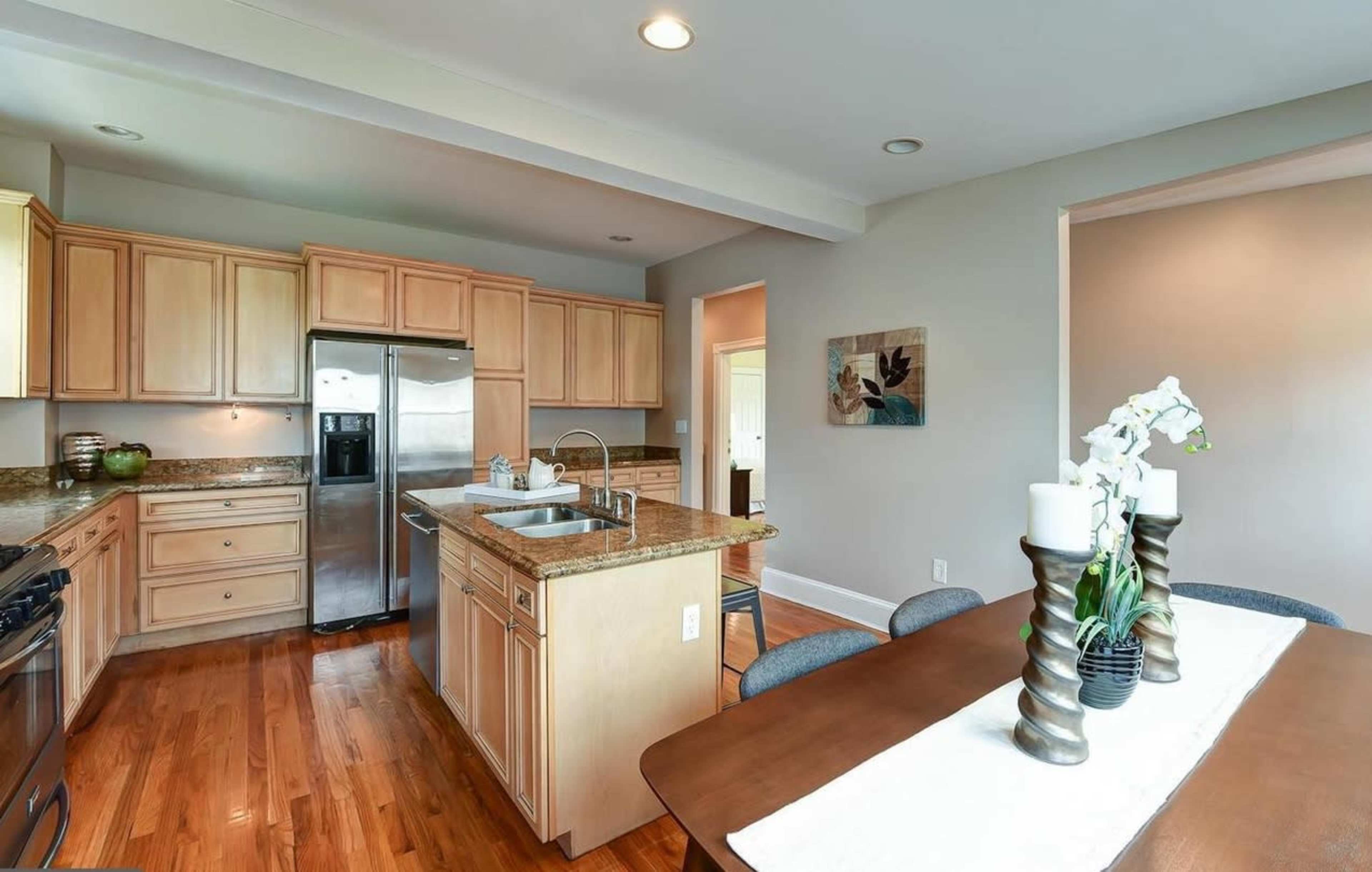 A modern kitchen with wooden cabinets, granite countertops, stainless steel appliances, and a dining area featuring a table with decorative items.