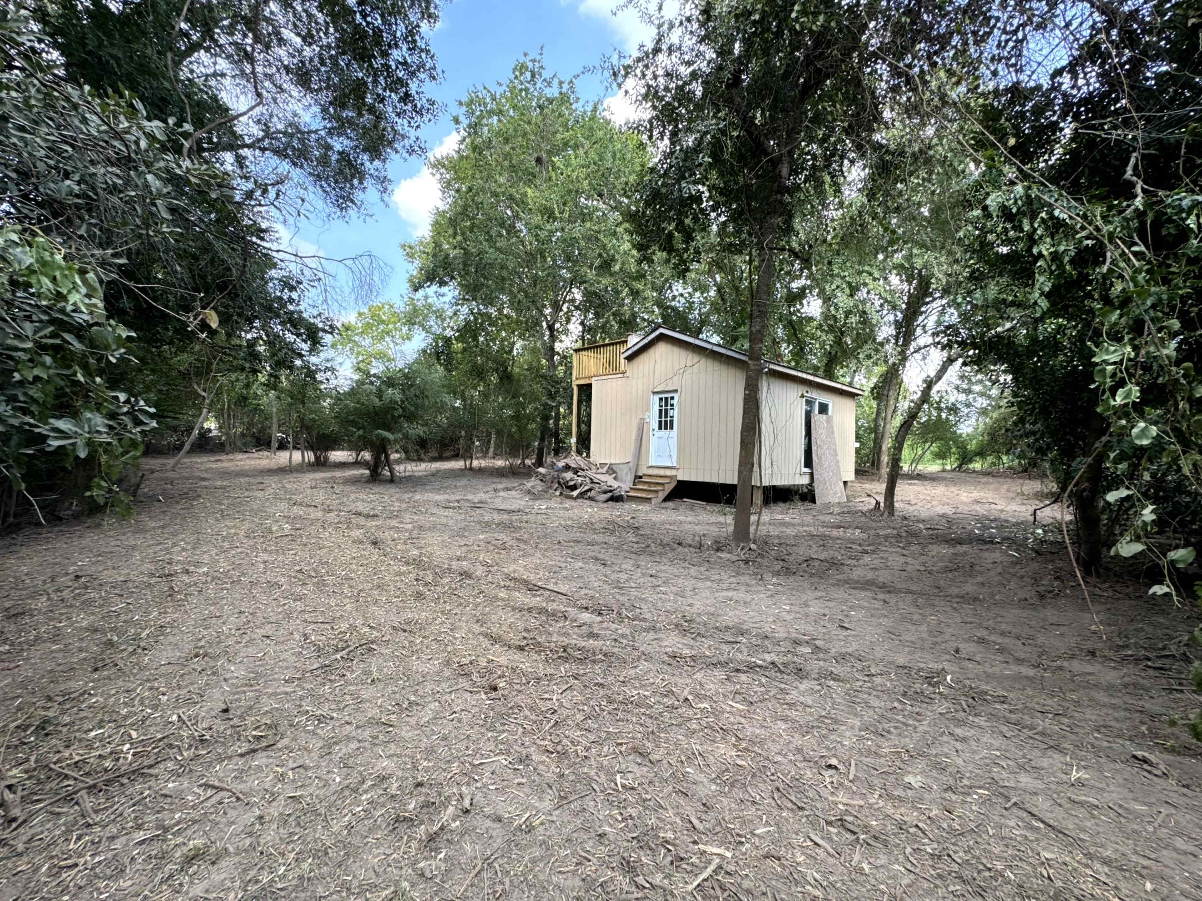 A small wooden cabin is set amidst a cleared area surrounded by trees and undergrowth.