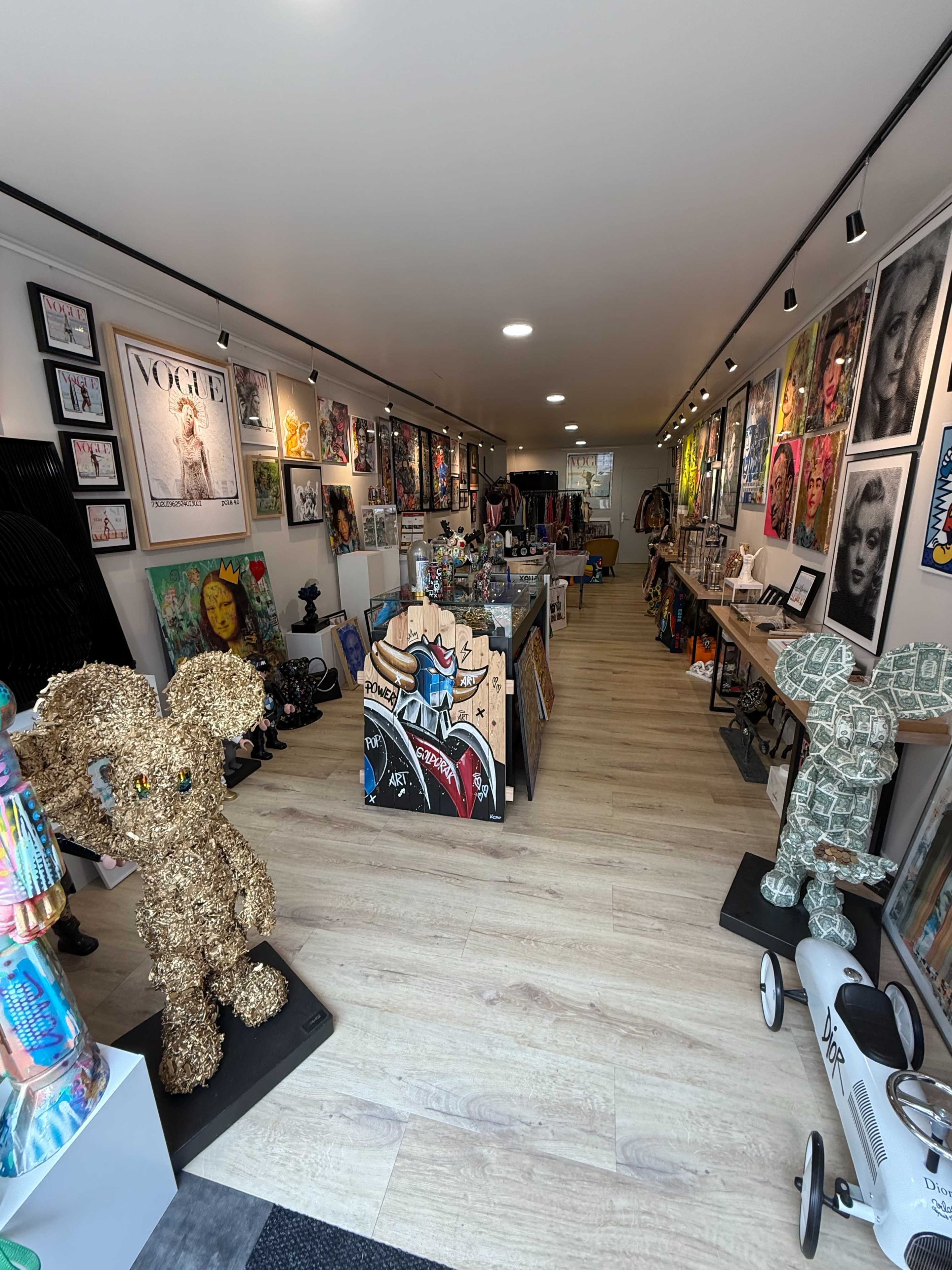 The image shows an art gallery interior filled with various artworks, sculptures, and colorful displays along the walls and central area.