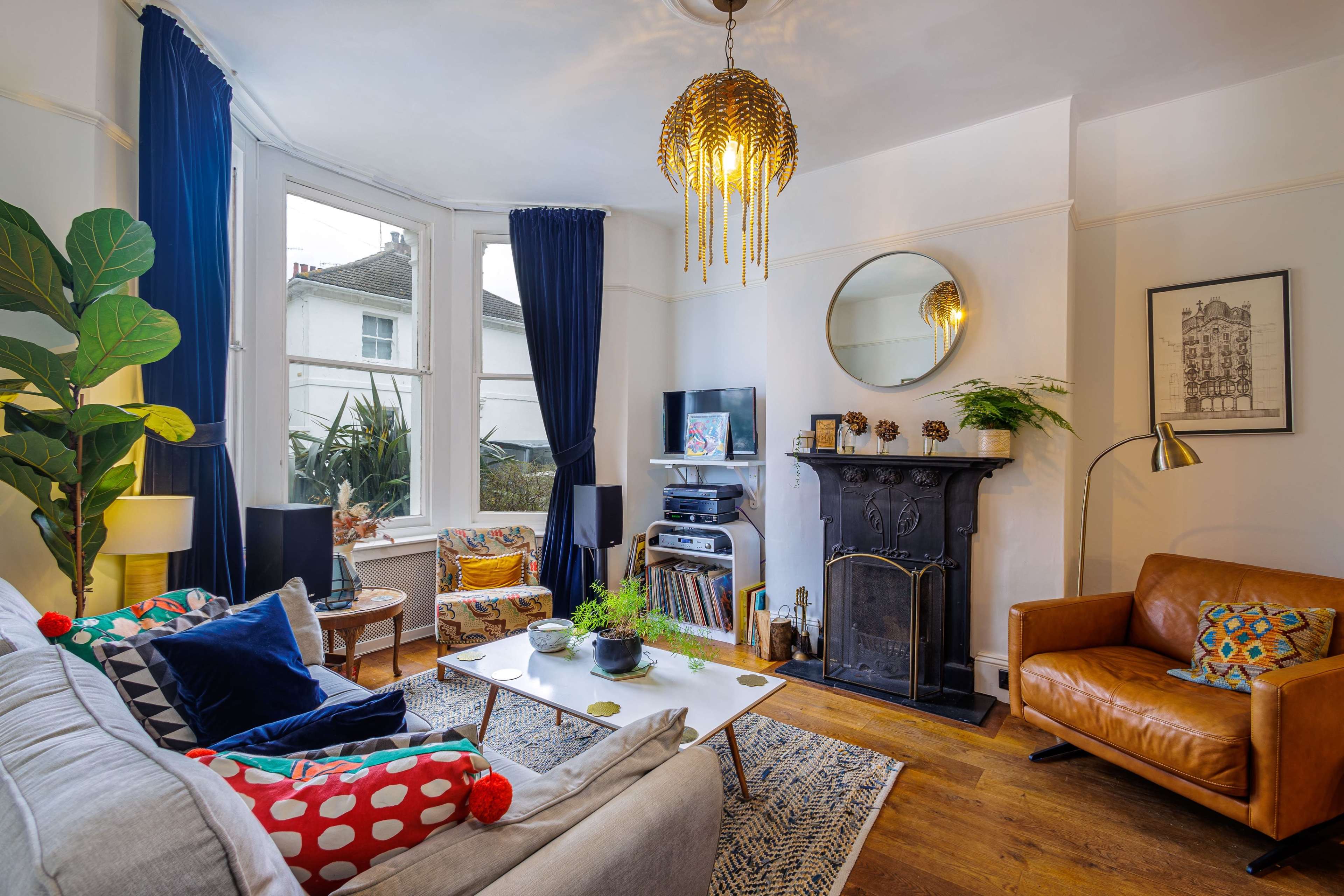 The living room features a mix of comfortable seating, a fireplace, and large windows with blue curtains, creating a cozy atmosphere.