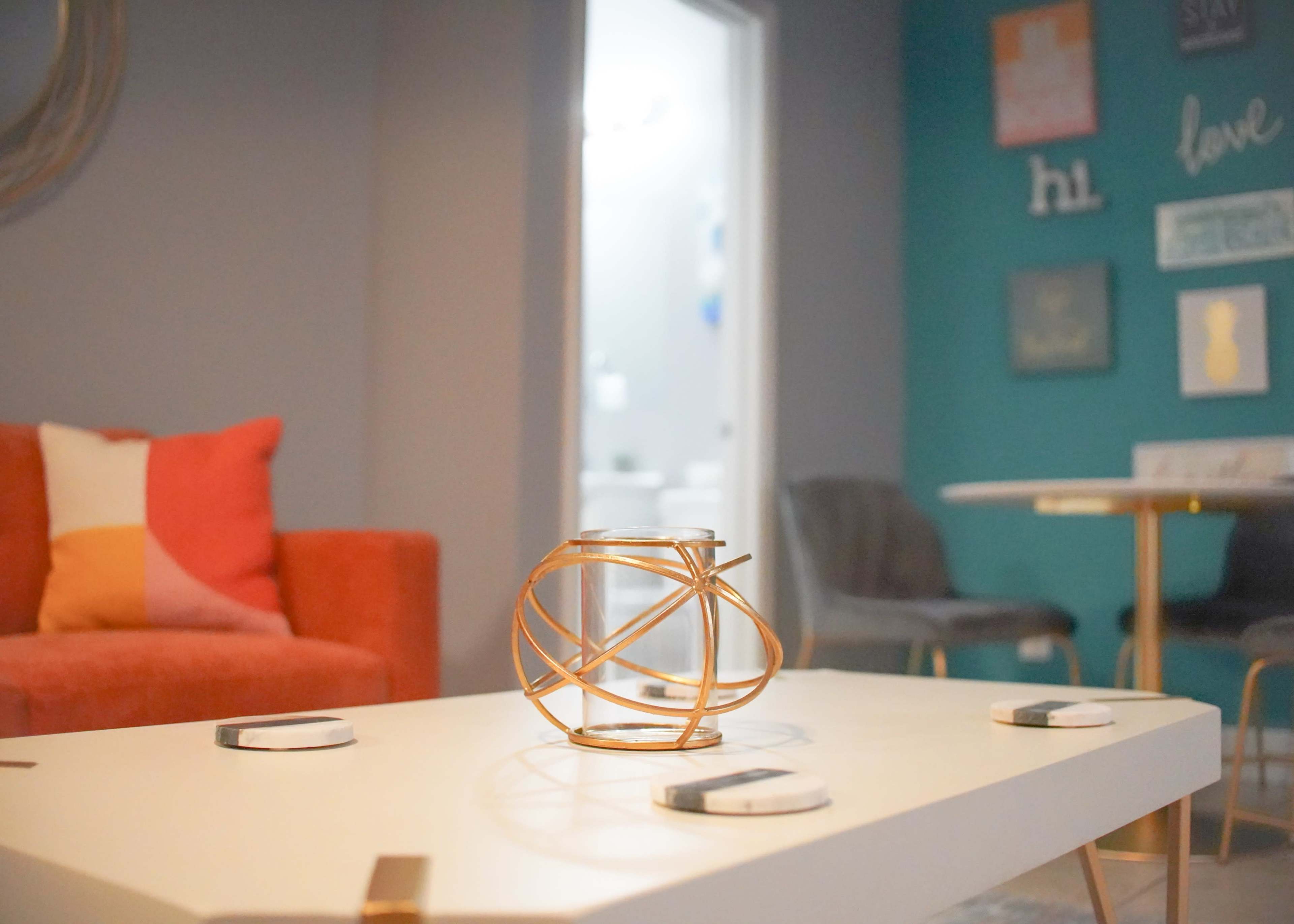 A coffee table with a decorative centerpiece is positioned in a living room featuring a red and white sofa and a teal wall with framed art.