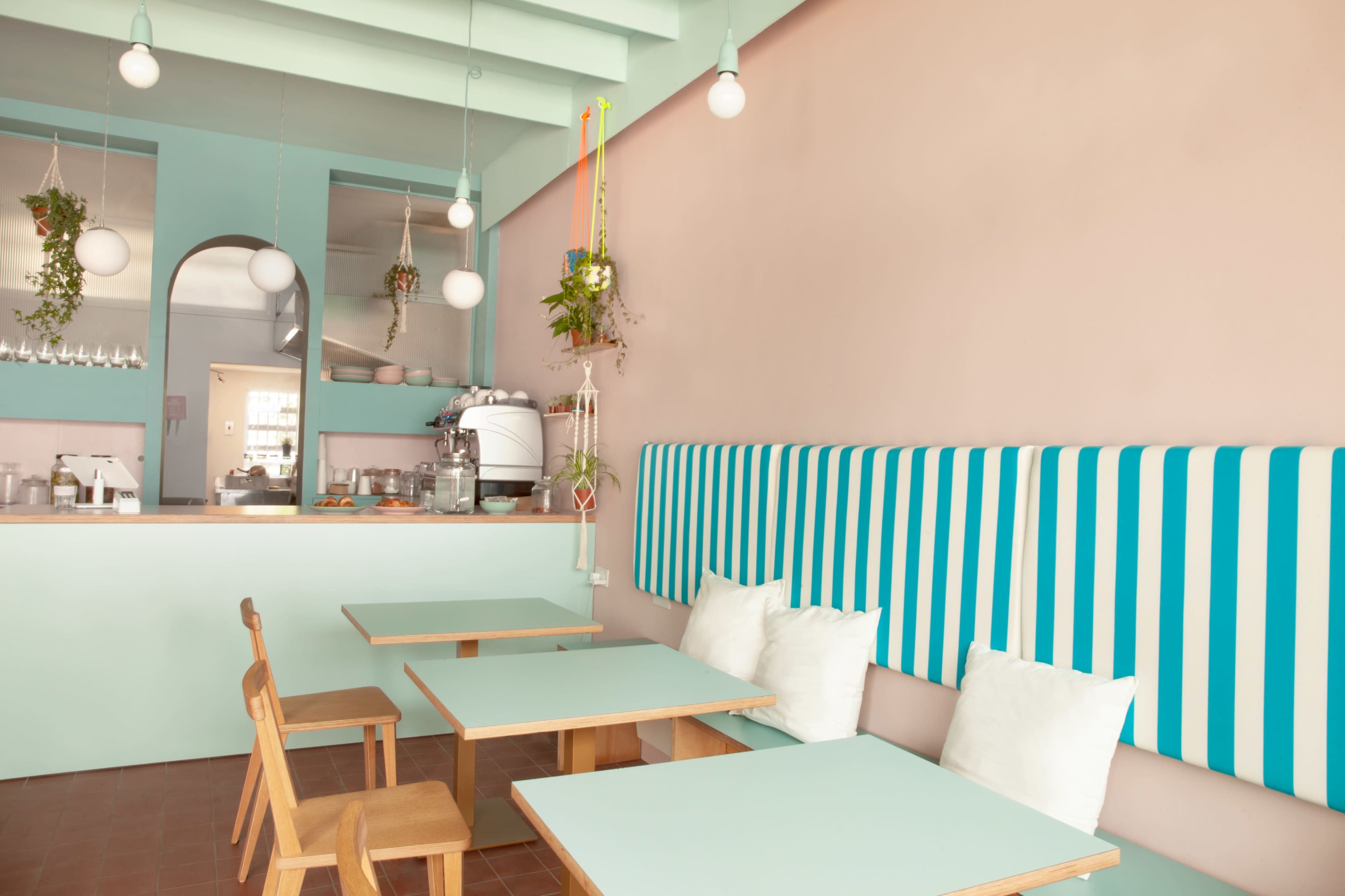 A brightly colored café interior featuring mint green and pink walls, striped seating, and wooden tables with white cushions.