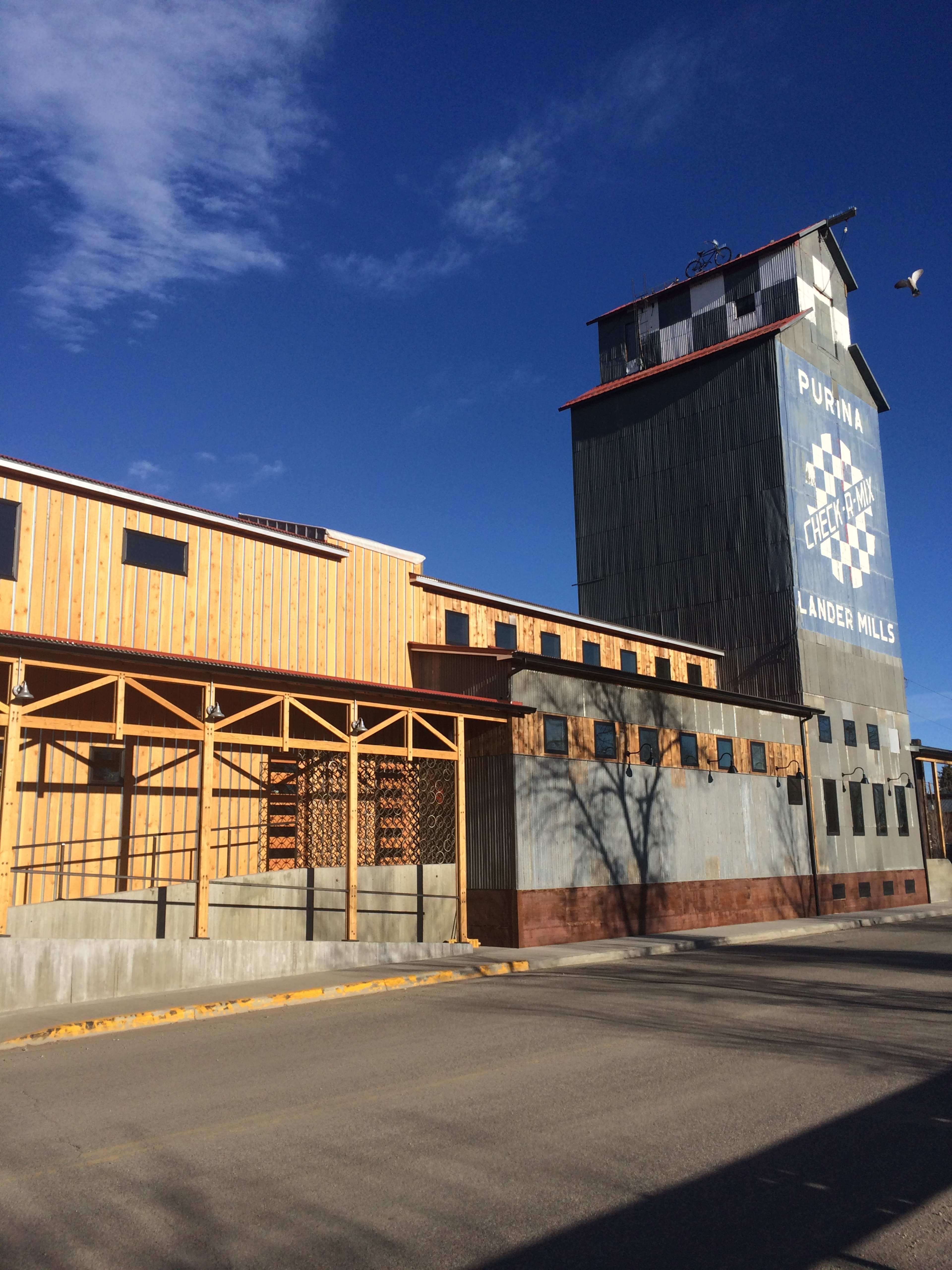 A large, multi-story building with a weathered metal facade and a wooden structure, featuring a sign that reads "PURINA" and "CHEESE FACTORY LANDER MILLS."