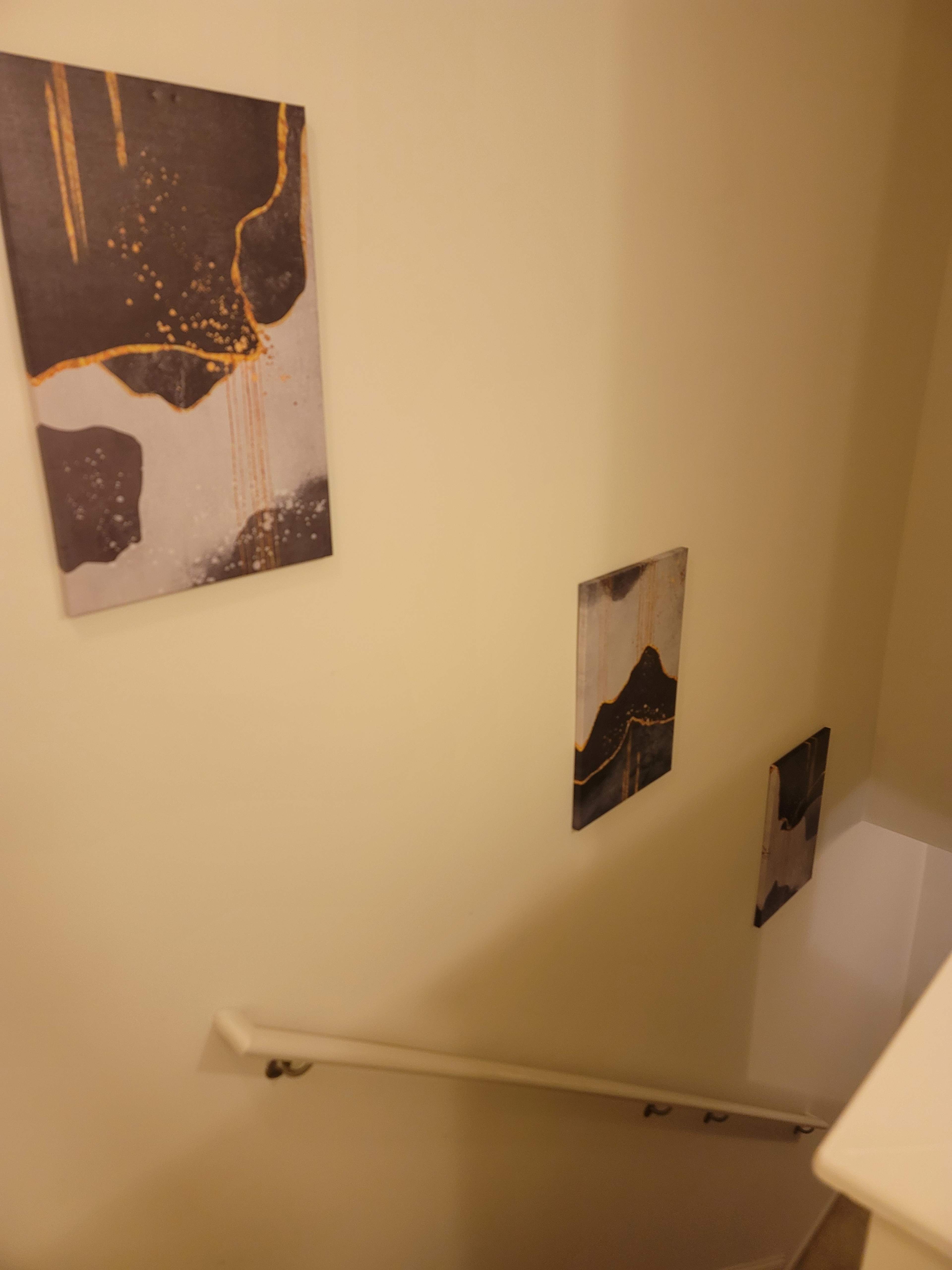 A downward staircase with three abstract paintings hanging on the wall.