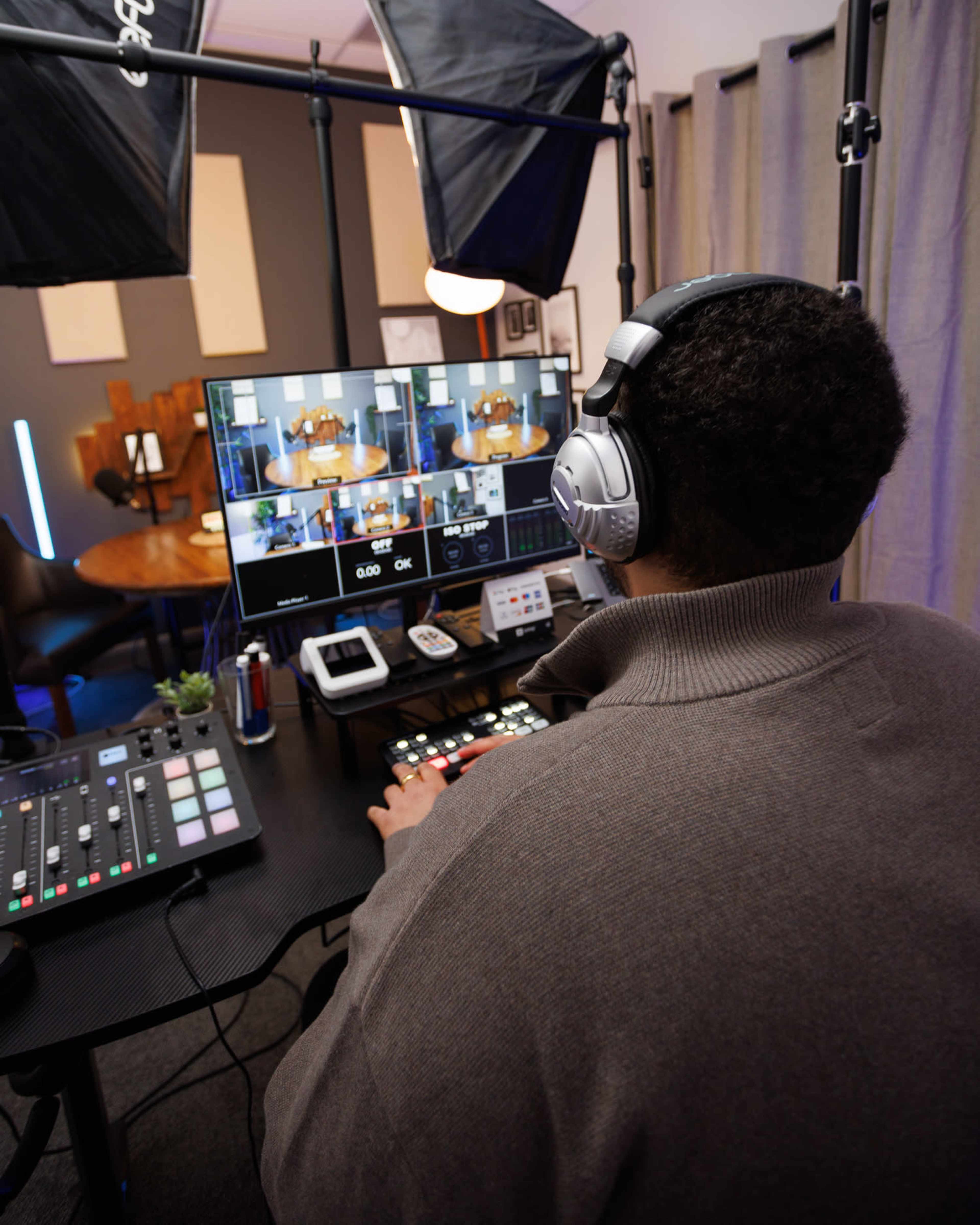 A person wearing headphones operates a video production setup with multiple screens and control equipment in a studio environment.