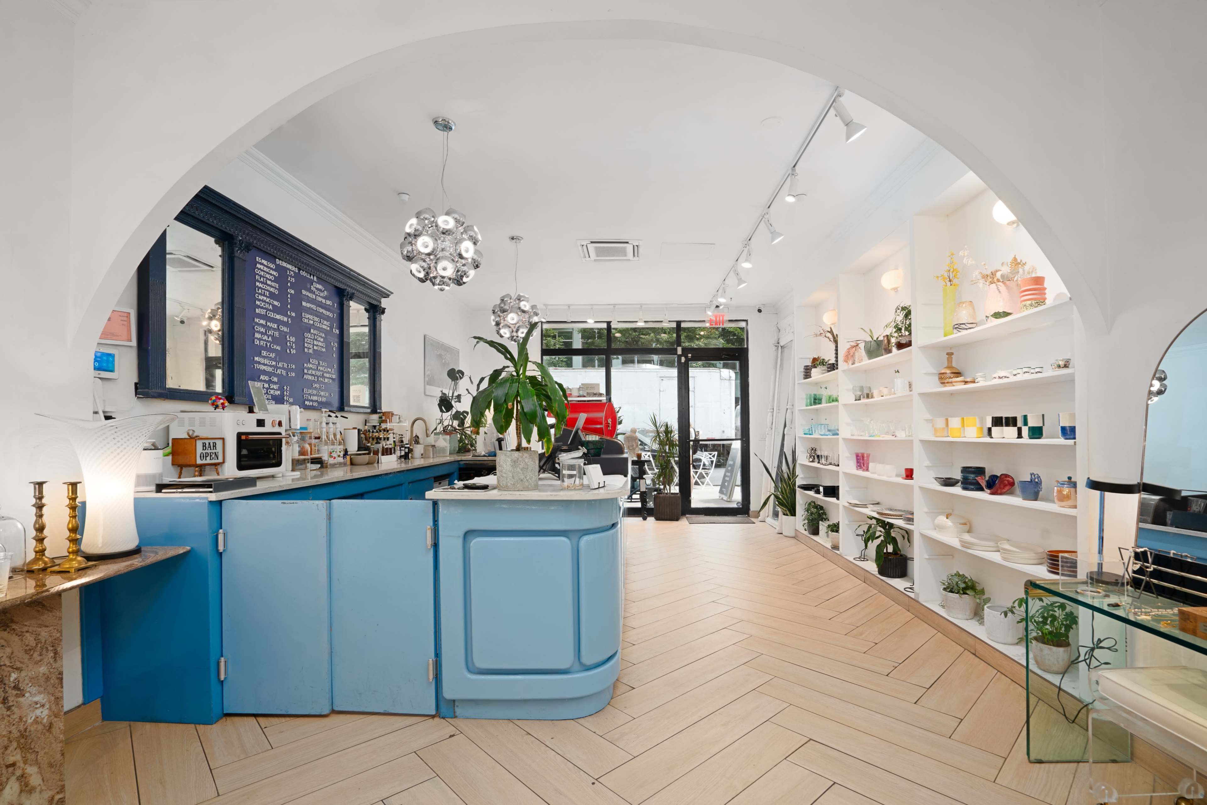 A bright, modern storefront features a blue counter with plants and shelves lined with various colorful items.