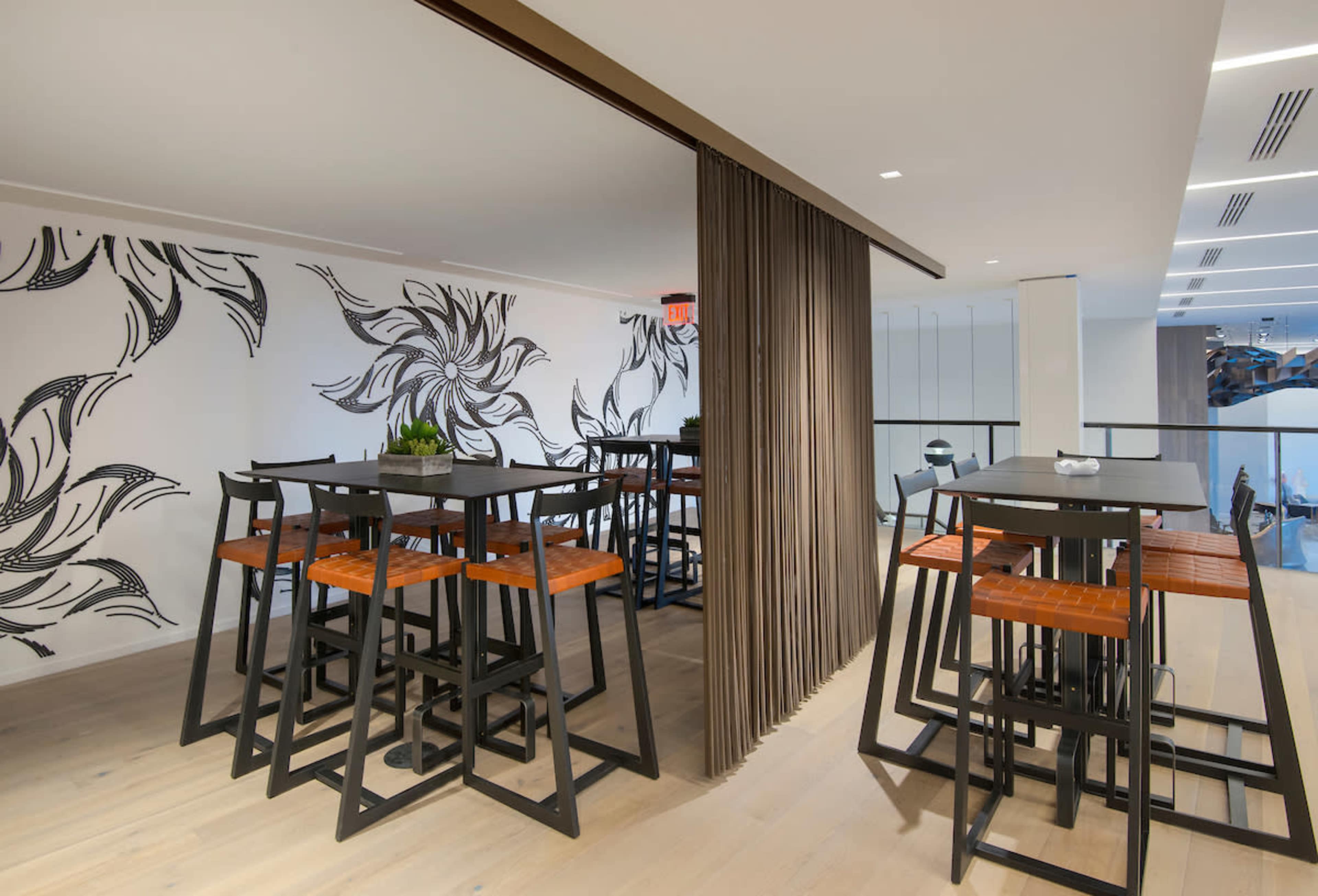 A modern dining area with tall tables and chairs, featuring a decorative floral mural on the wall.