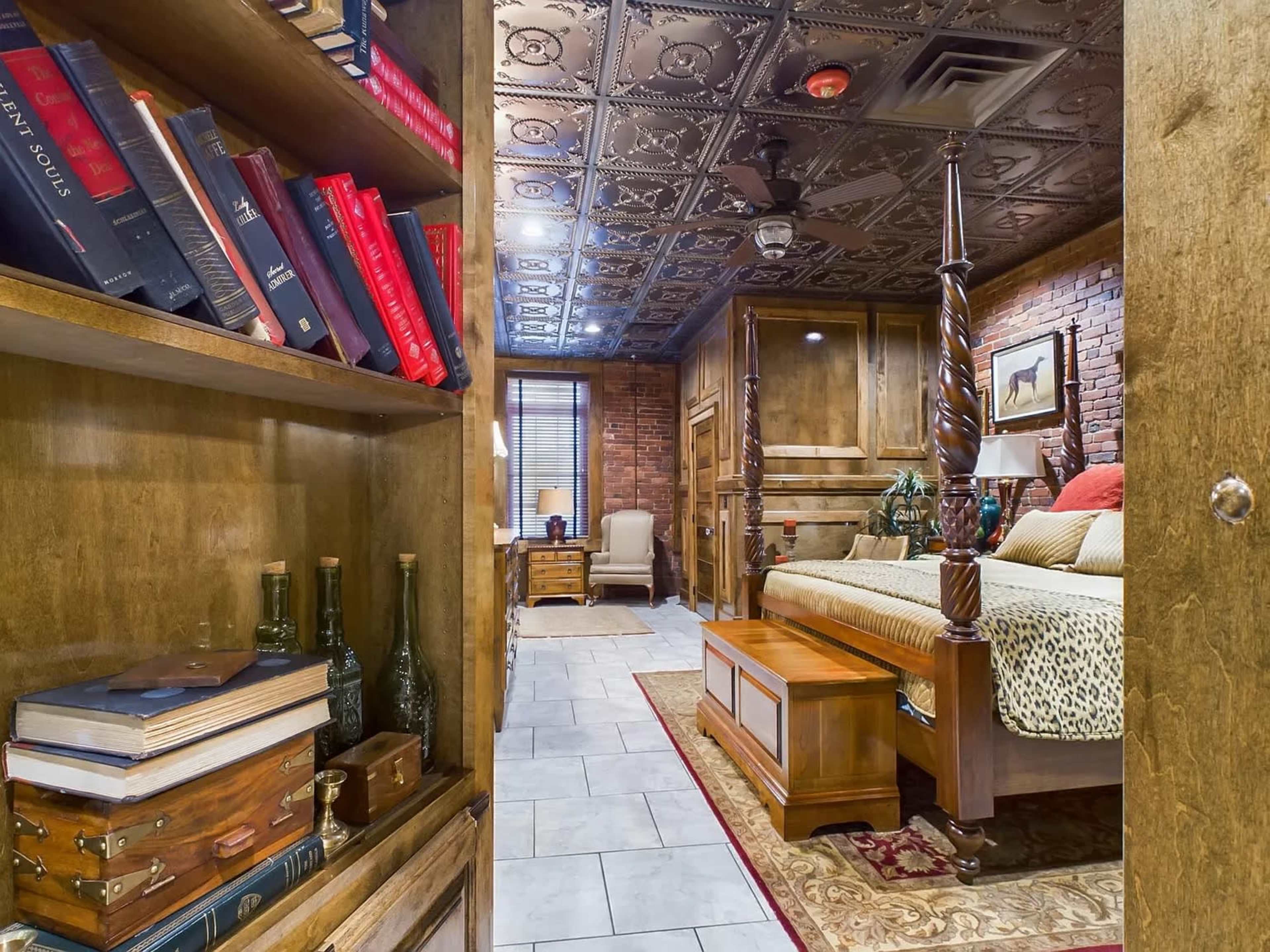 The image shows a view of a bedroom featuring a decorative ceiling, a large bed with a wooden frame, and bookshelves filled with various books and decorative items.