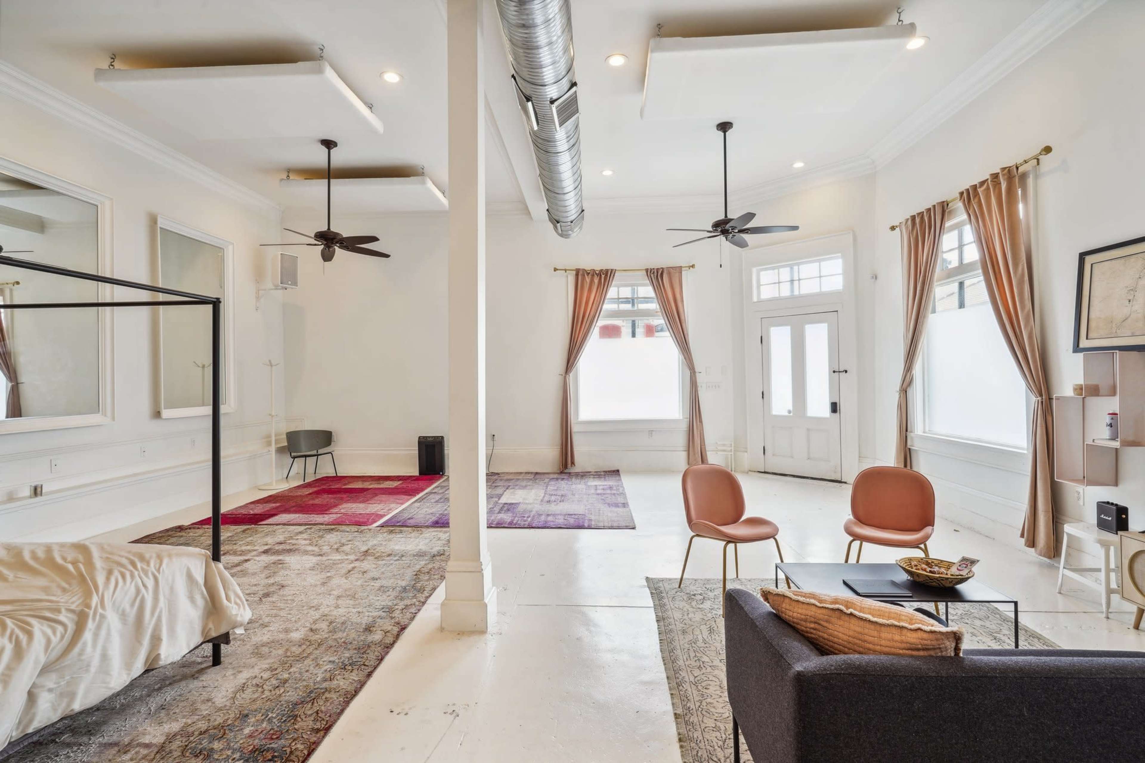 A spacious, minimally furnished room with large windows, two ceiling fans, and a mix of rugs on the polished floor.