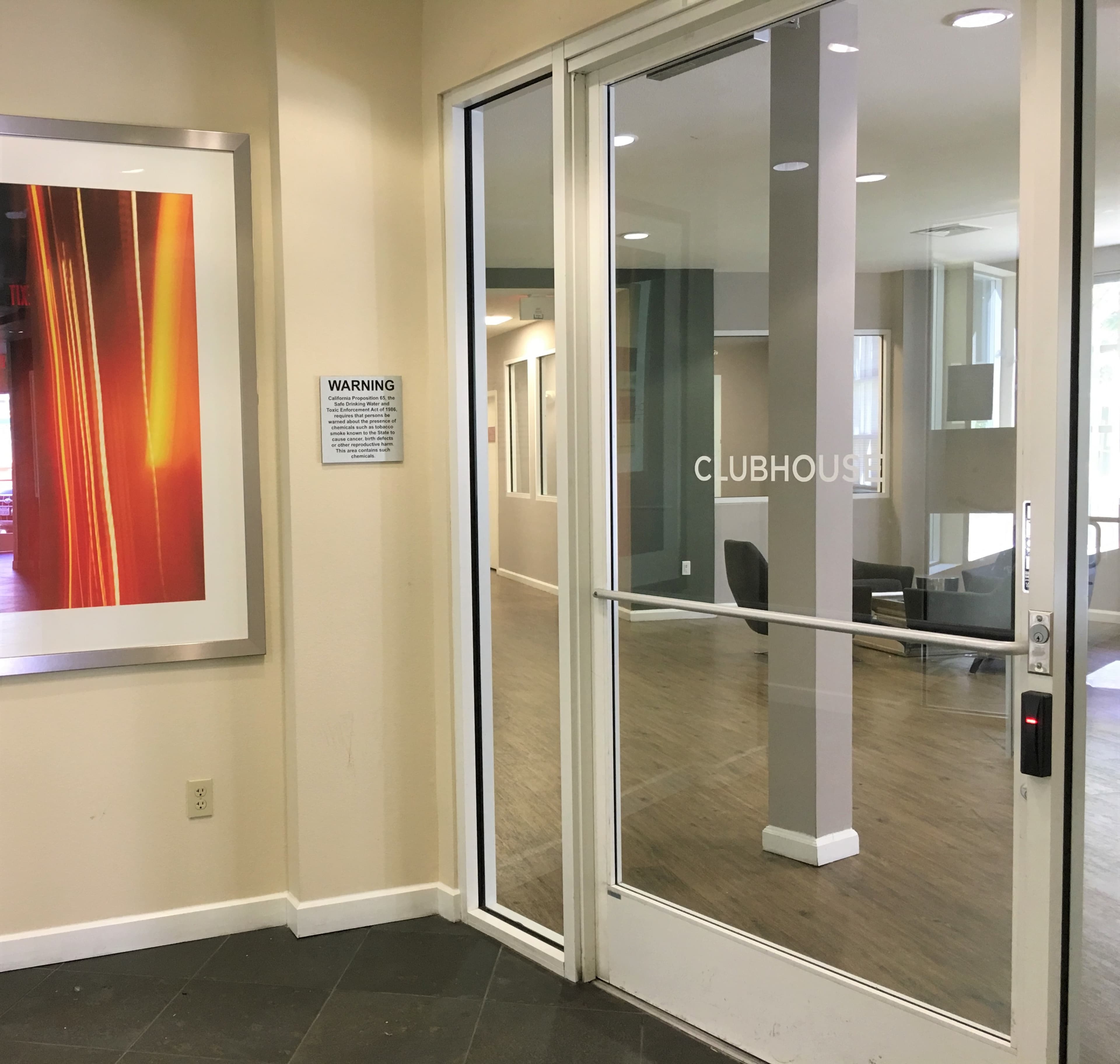 An entrance to a clubhouse with glass doors and a visible warning sign on the wall beside it.
