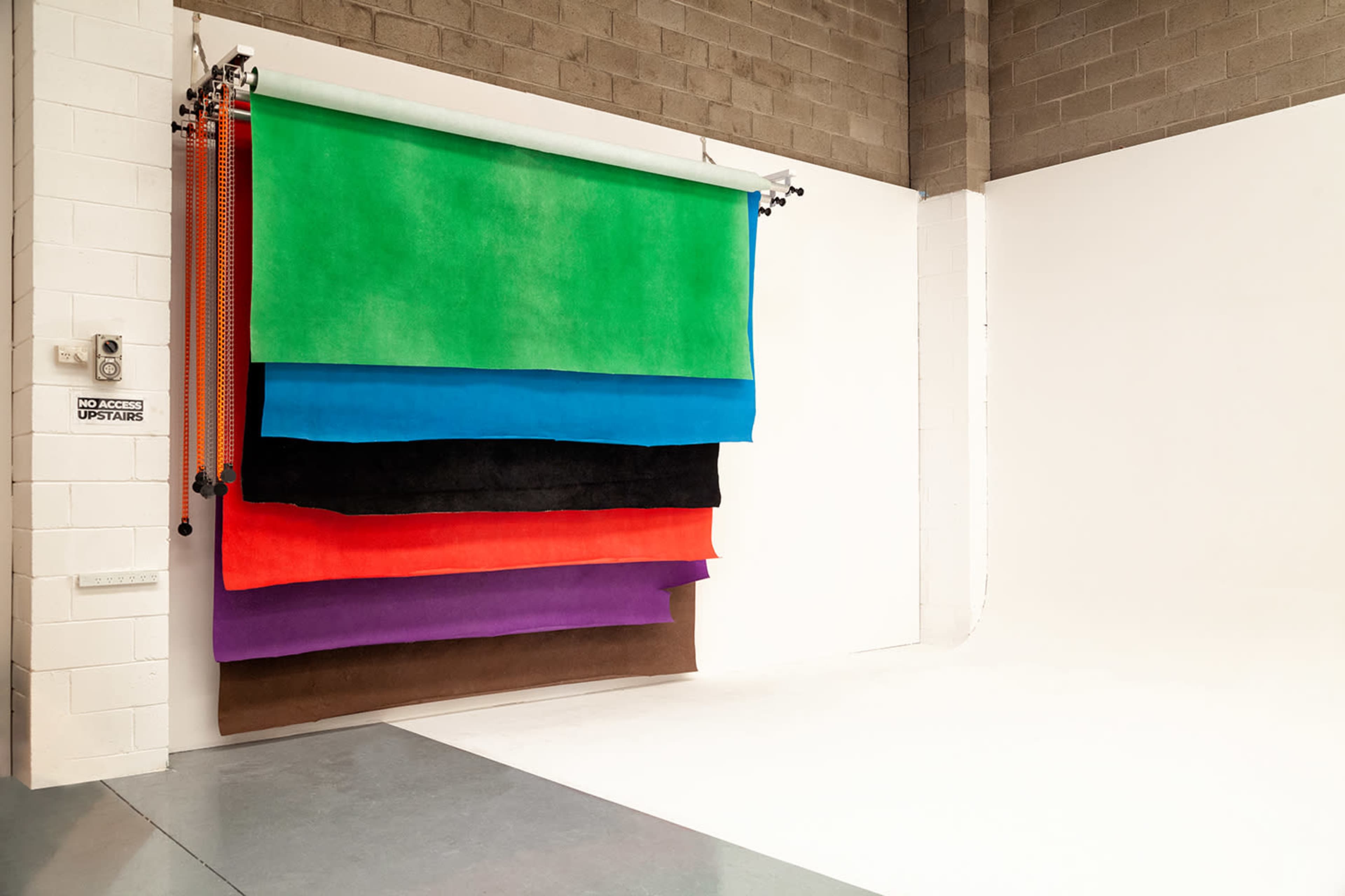 A studio backdrop setup with several colored fabric rolls arranged horizontally against a white wall.