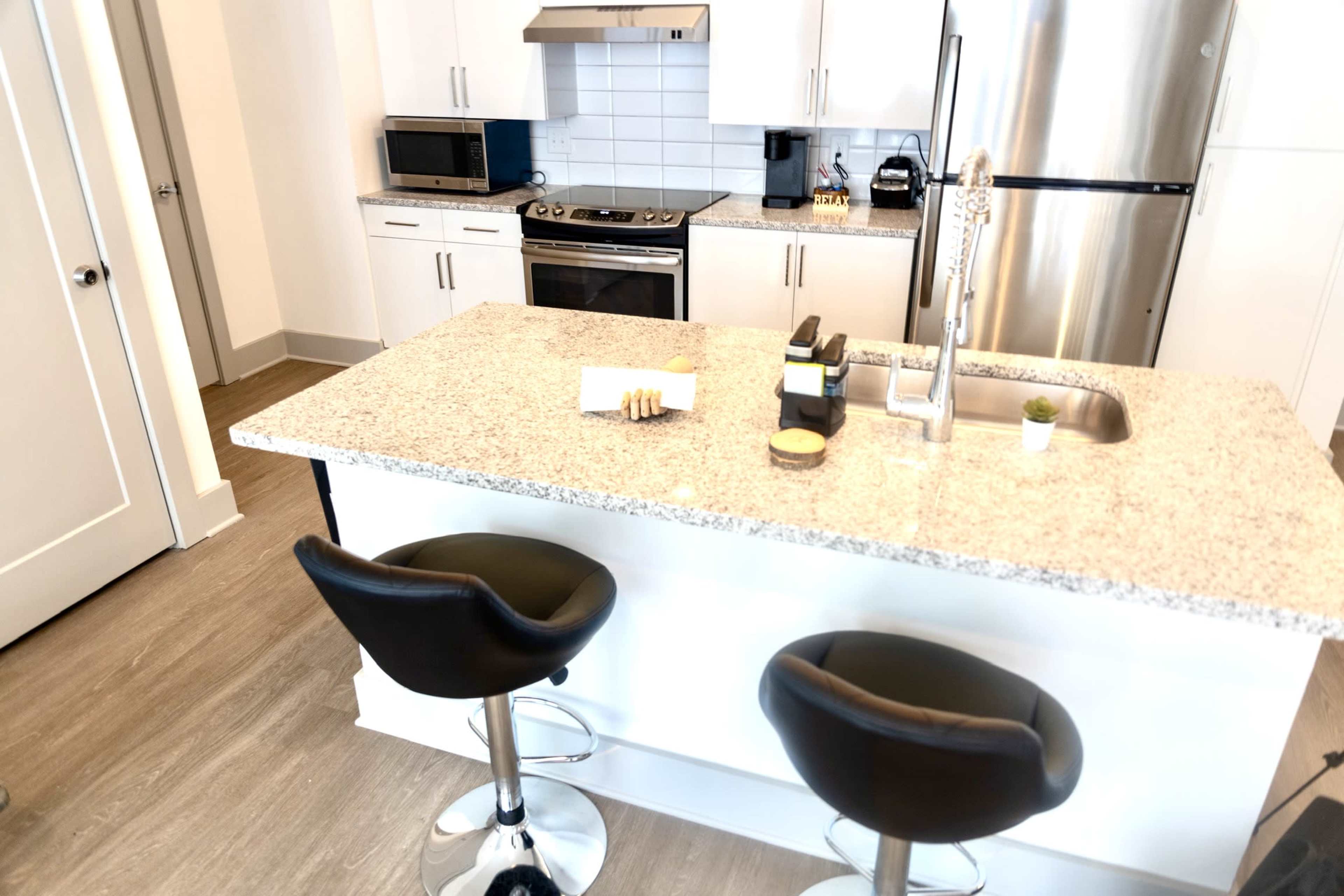 A modern kitchen features a central island with two black bar stools, stainless steel appliances, and a sleek countertop.