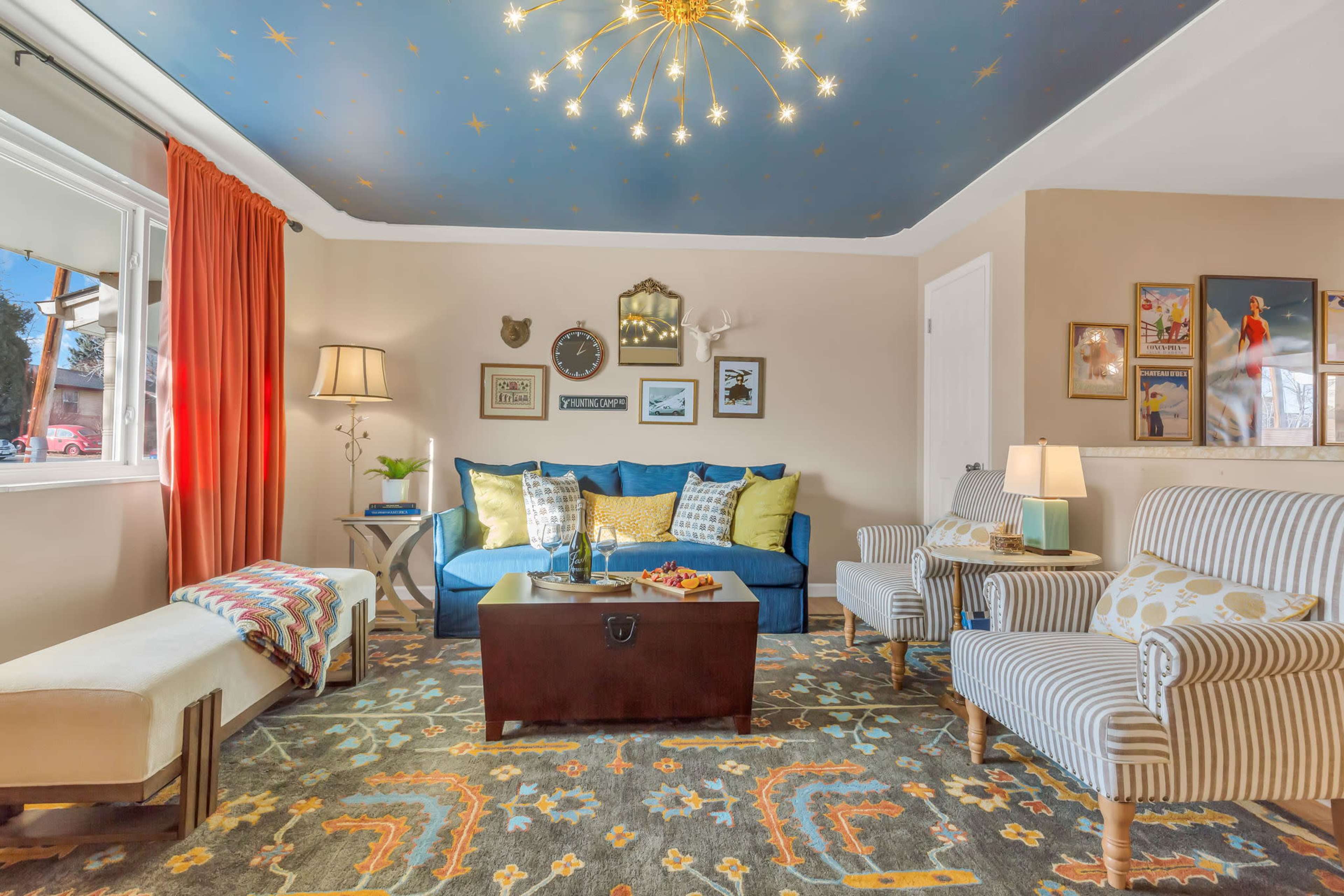 A living room with a blue sofa, two striped armchairs, a coffee table, and a ceiling designed with stars, complemented by a decorative rug and various wall artworks.