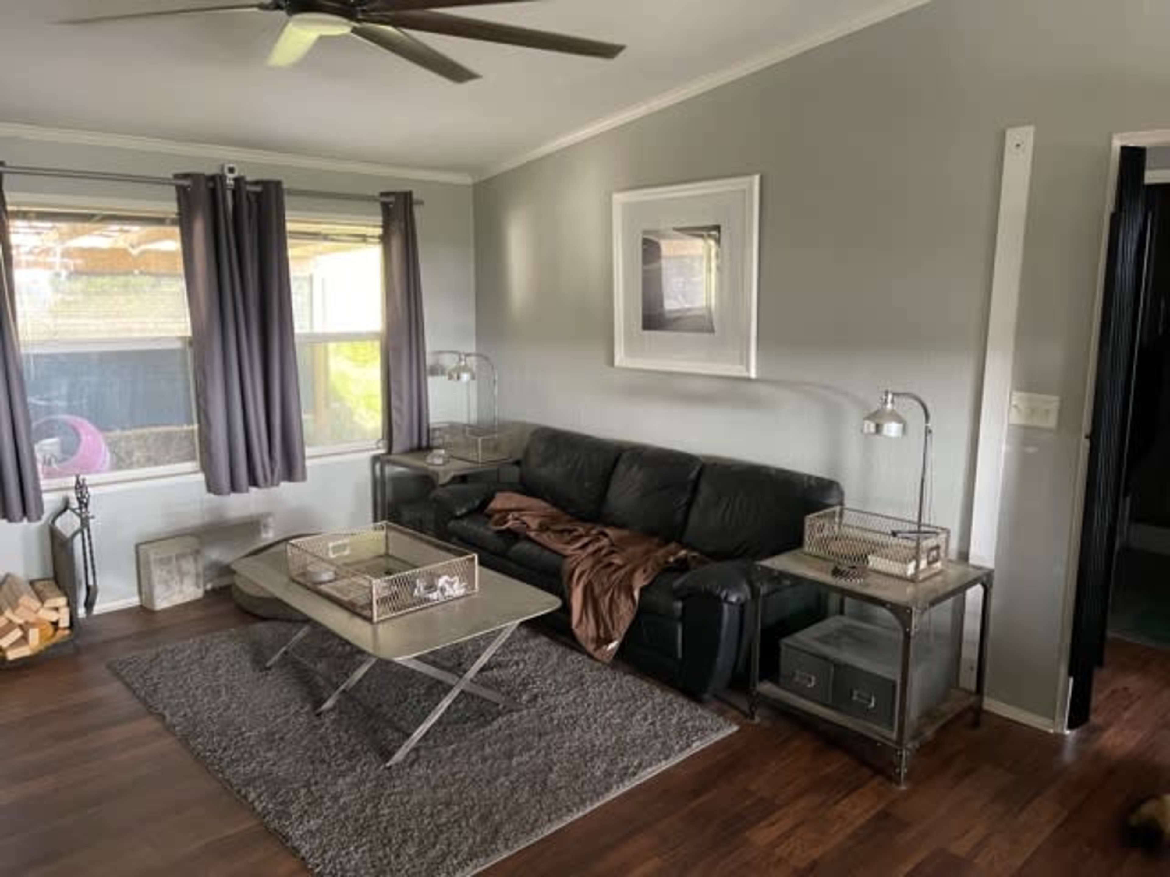 The image shows a living room with a black leather sofa, a coffee table, and two side tables, all set against gray walls and hardwood flooring.
