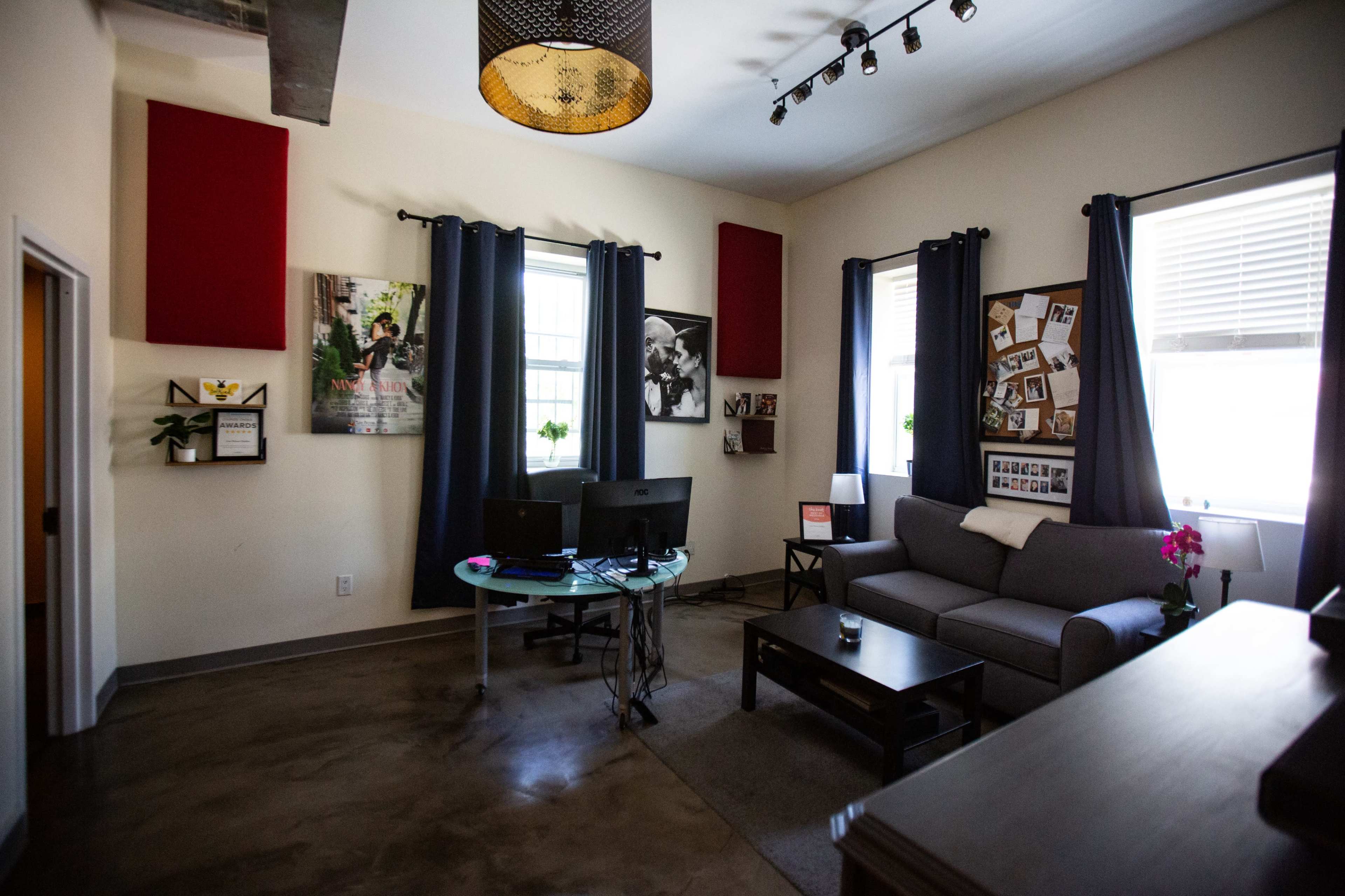 A modern living room featuring a gray sofa, a coffee table, two computer monitors, and framed photographs on the walls.