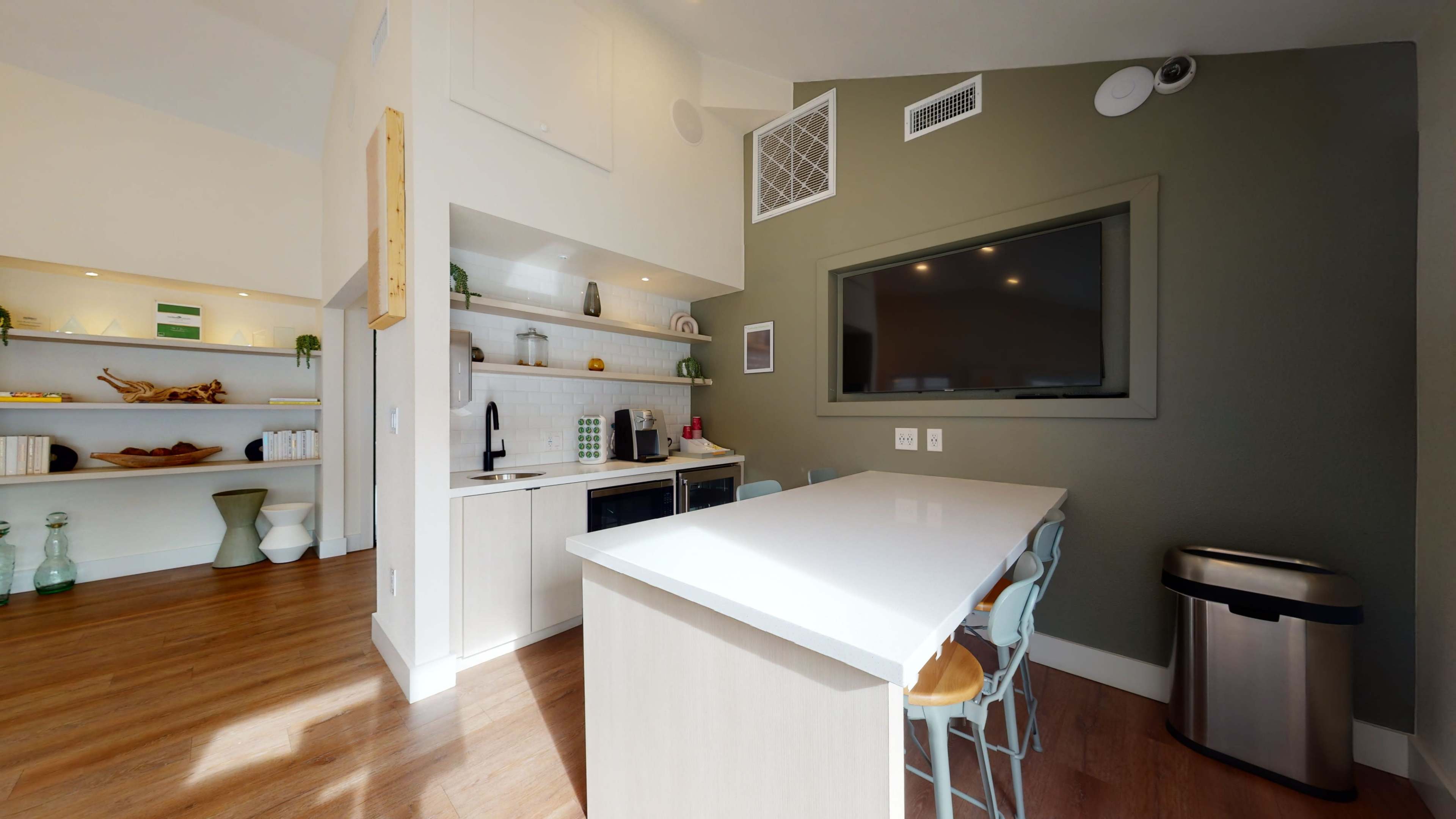 A modern kitchen with a white island, cabinetry, and a large window, featuring shelves with decorative items.