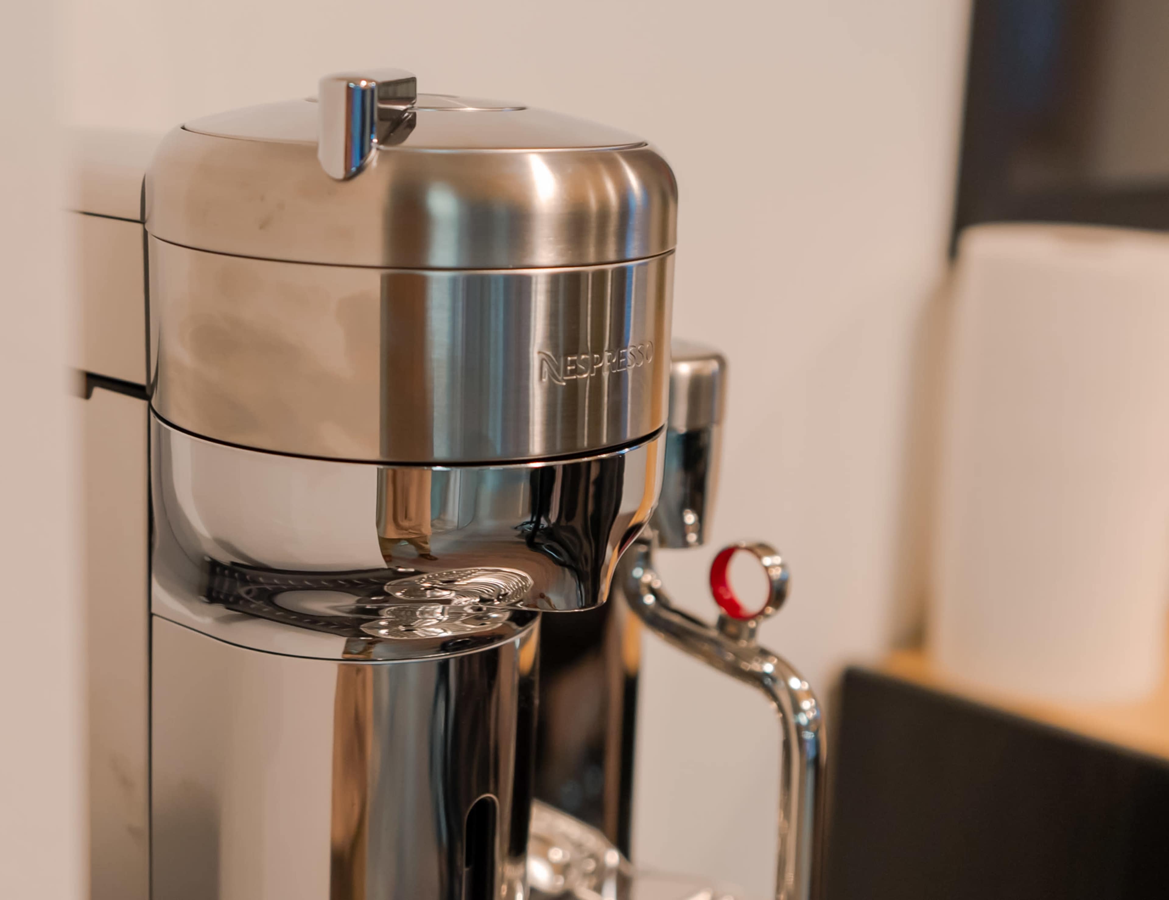 A Nespresso coffee machine with a sleek, metallic design placed near a roll of paper towels.