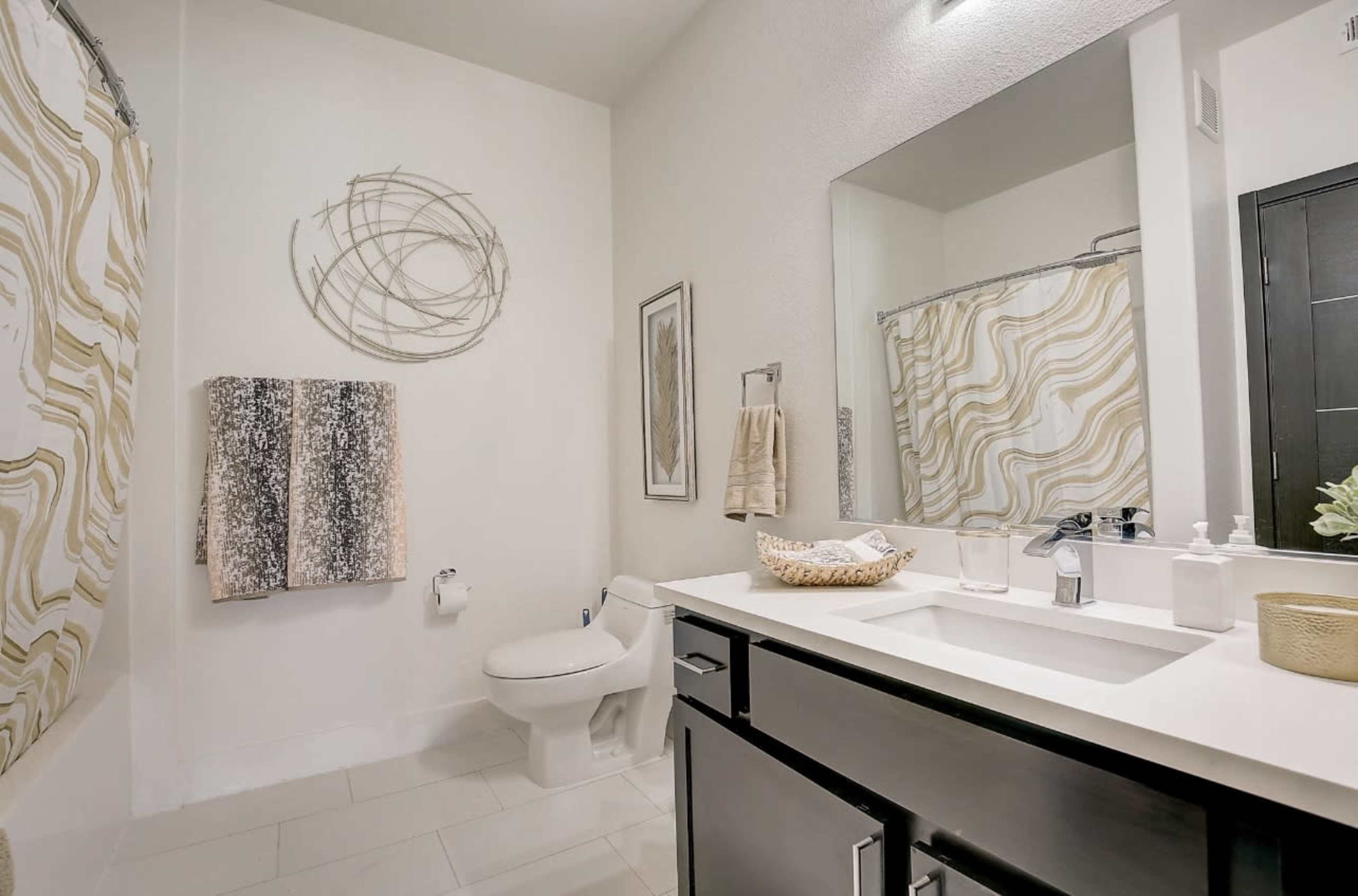 A modern bathroom with a white color scheme, featuring a toilet, a sink with a mirror, and decorative towels hanging on the wall.