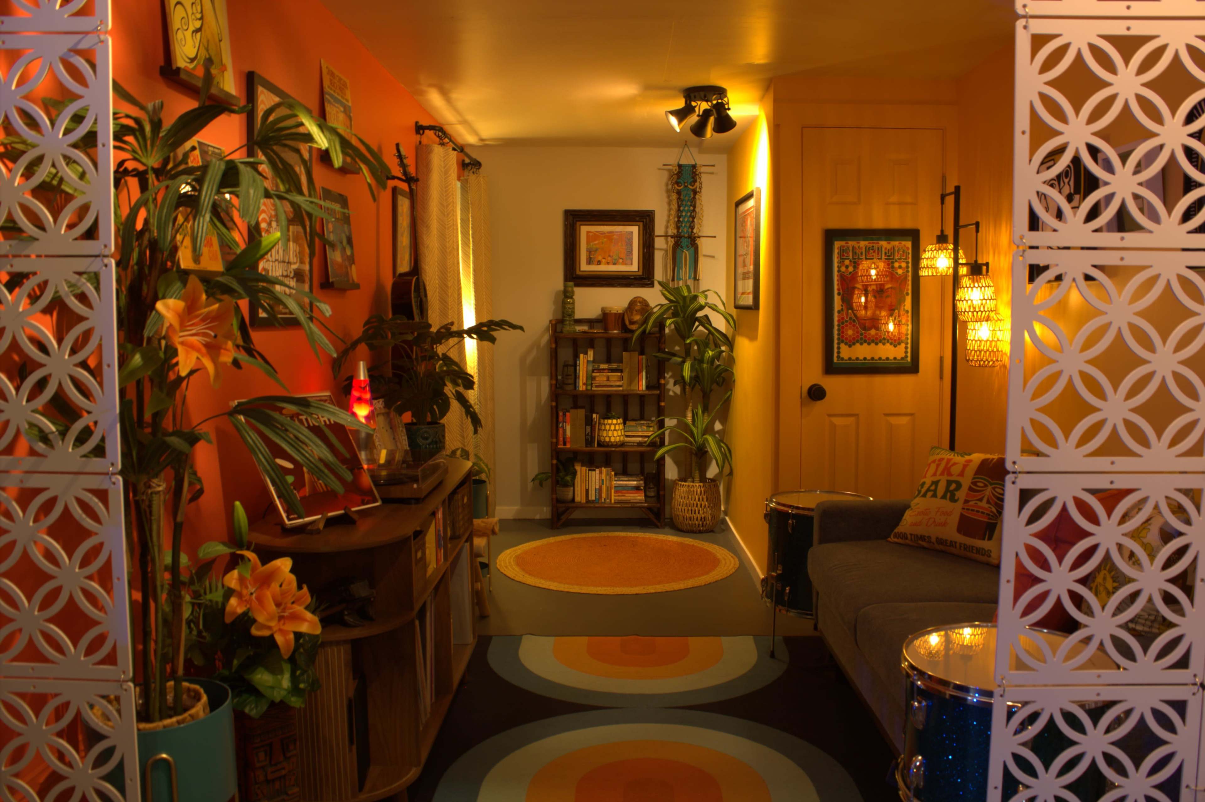 The image shows a vibrant interior space with orange walls, a cozy seating area, plants, and colorful decor.