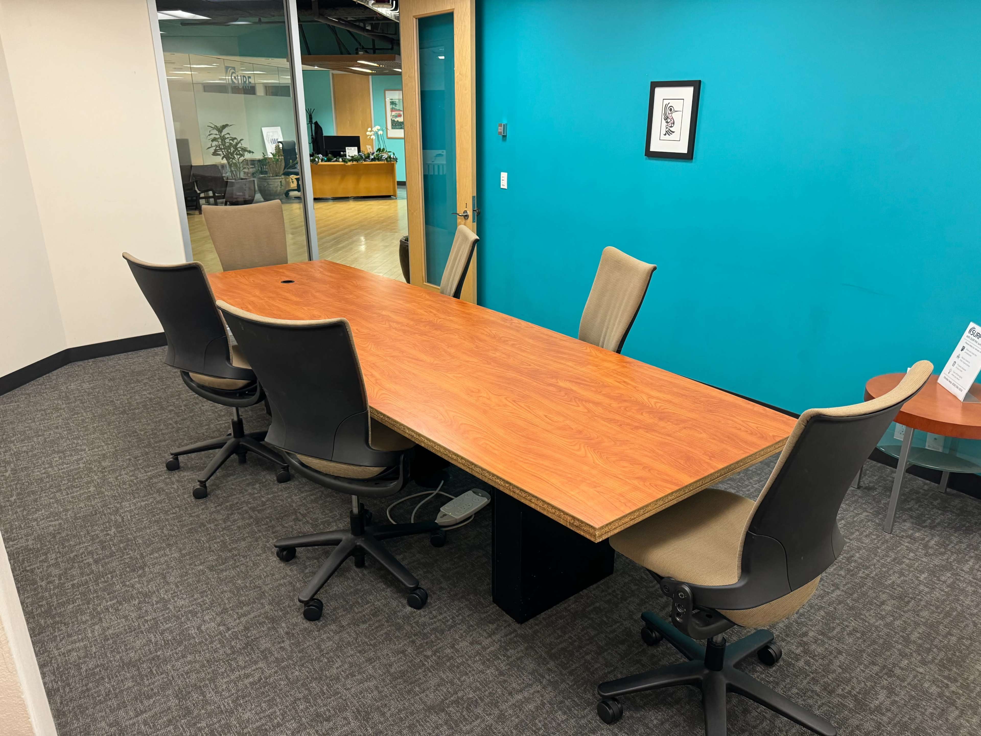 A large wooden conference table is surrounded by five office chairs in a room with teal walls.
