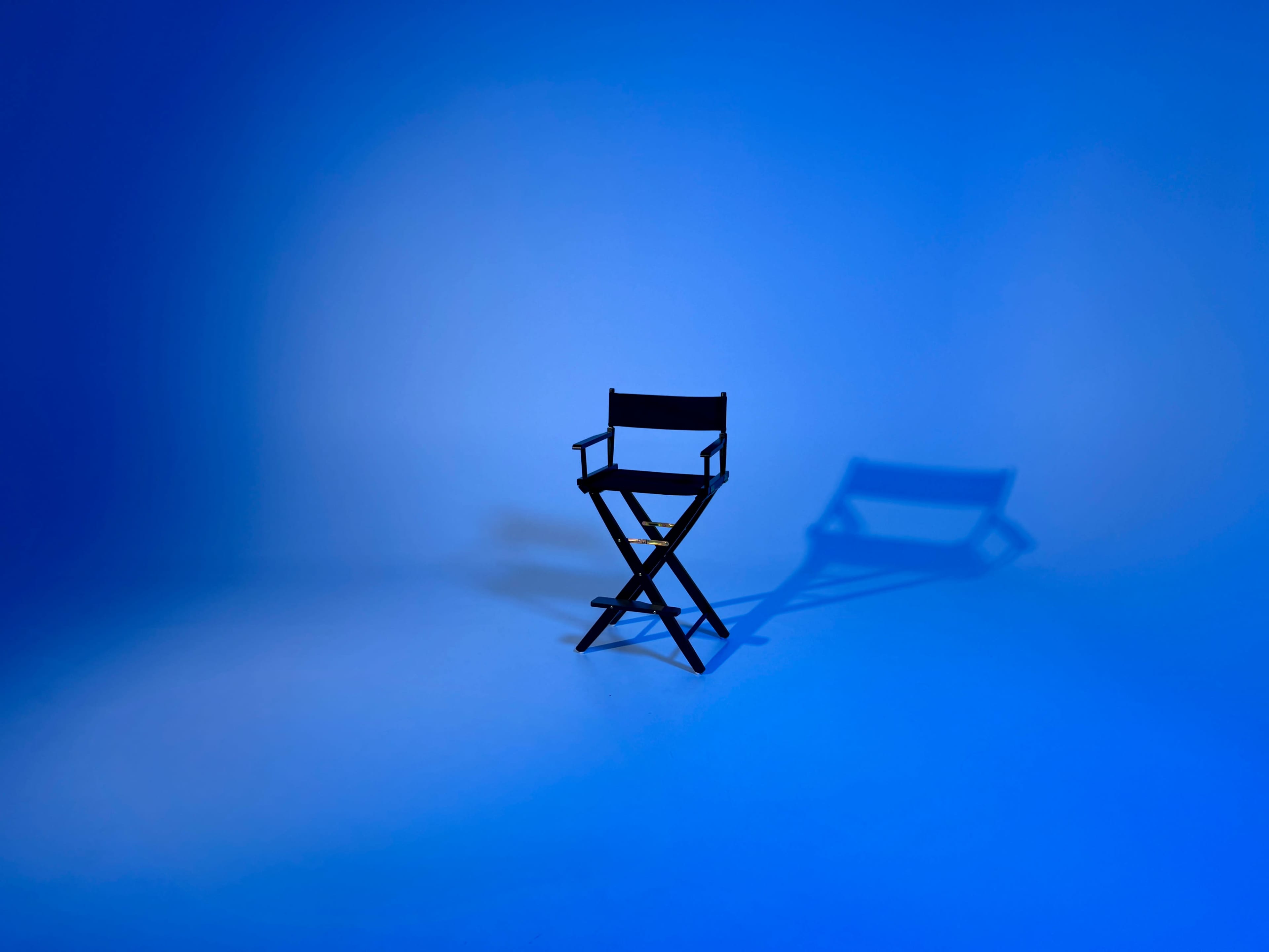 A black director's chair casts a shadow on a blue backdrop.